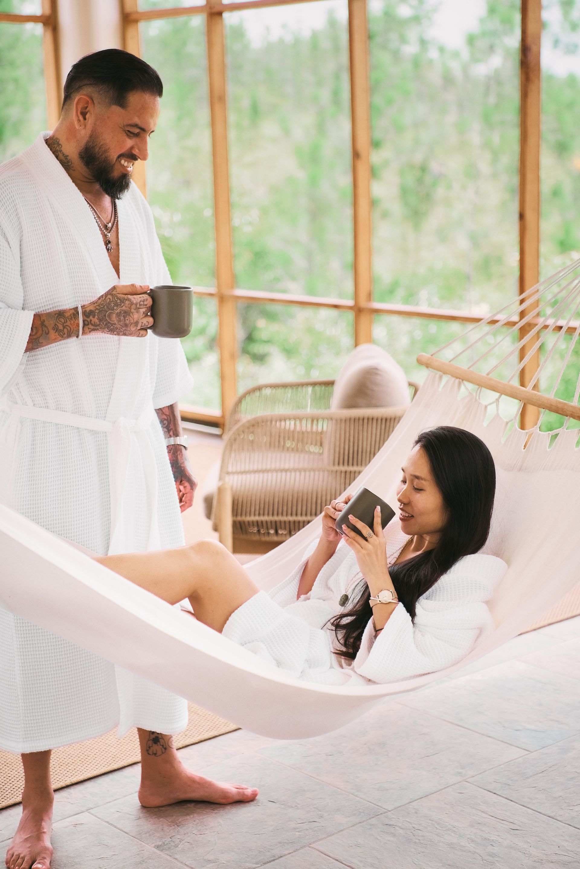 A man is standing next to a woman in a hammock.