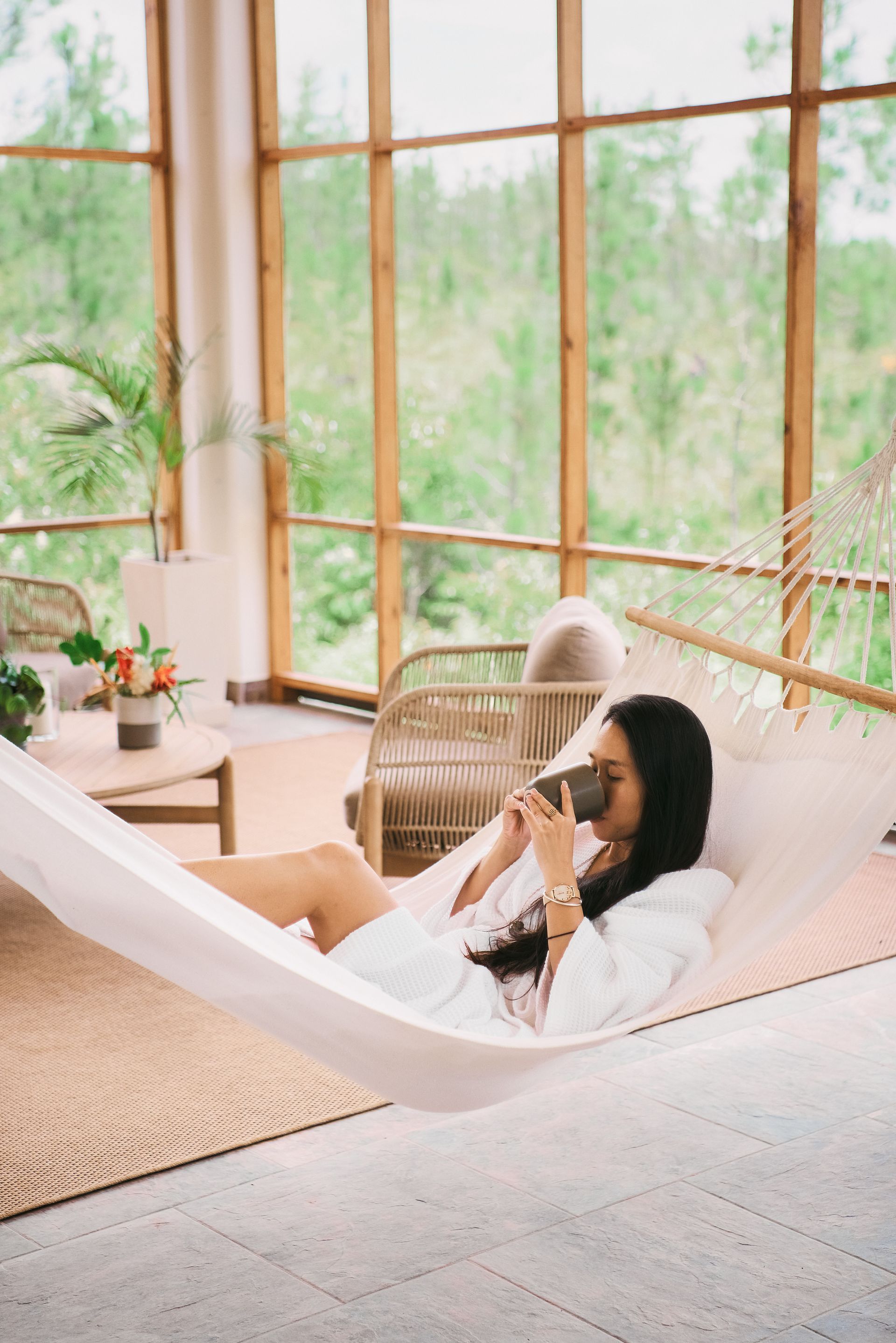 A woman is laying in a hammock drinking a cup of coffee.