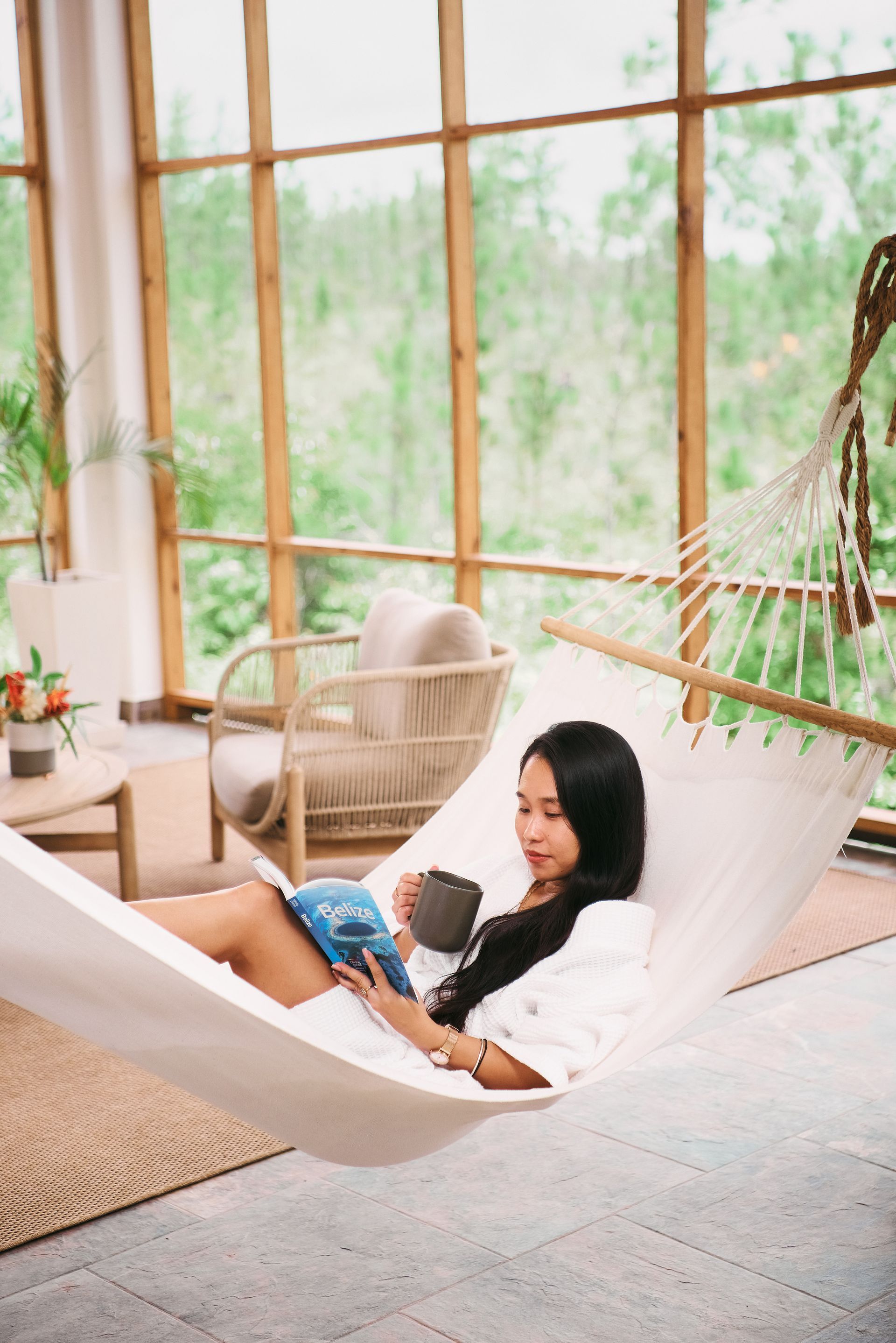 A woman is laying in a hammock reading a book.