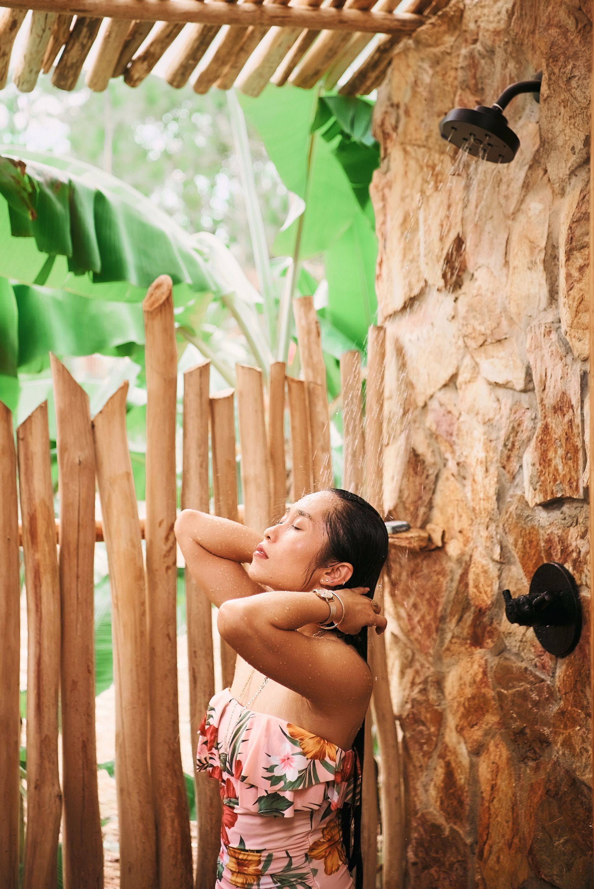 A woman is taking a shower under a wooden fence.