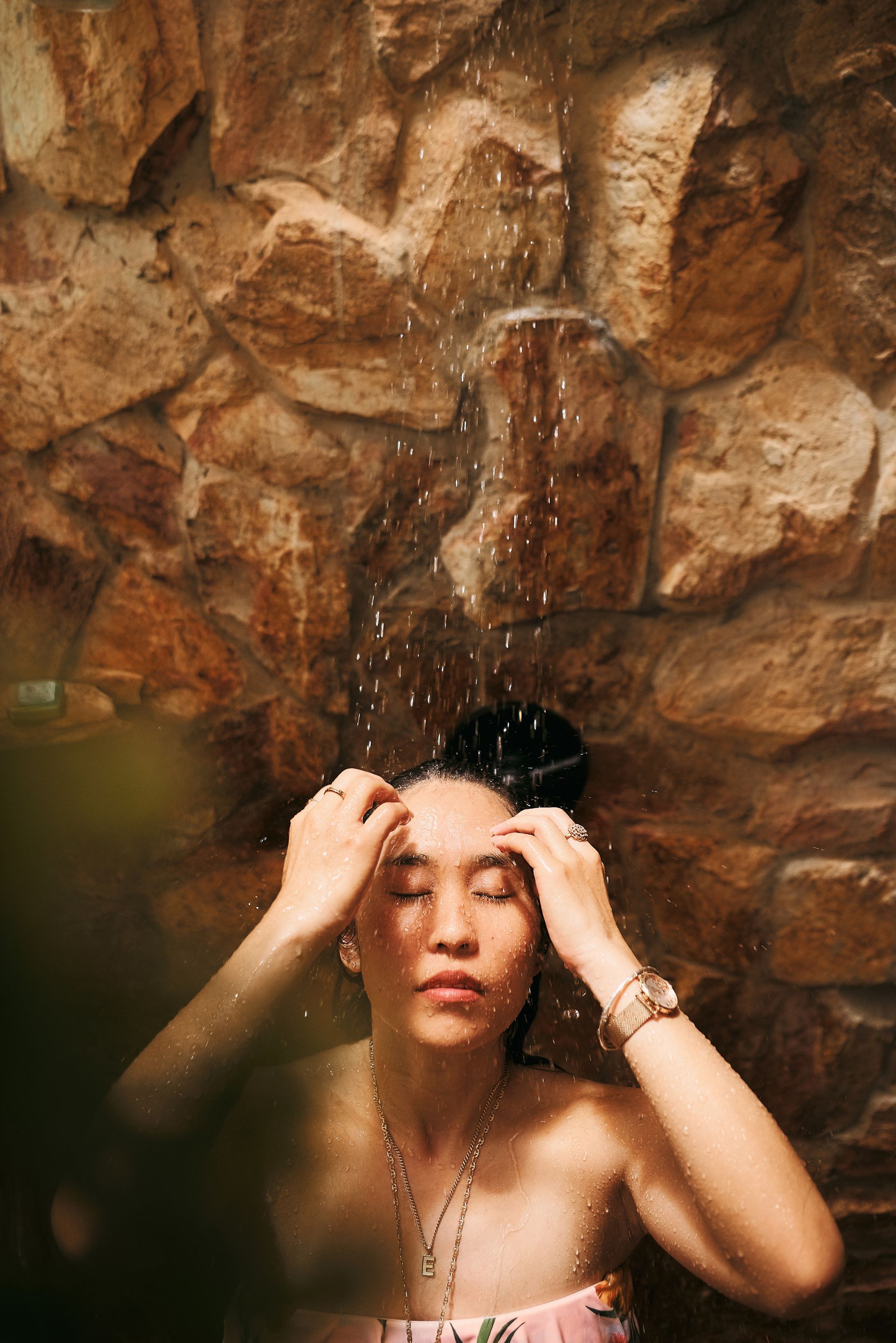 A woman is taking a shower in front of a stone wall.