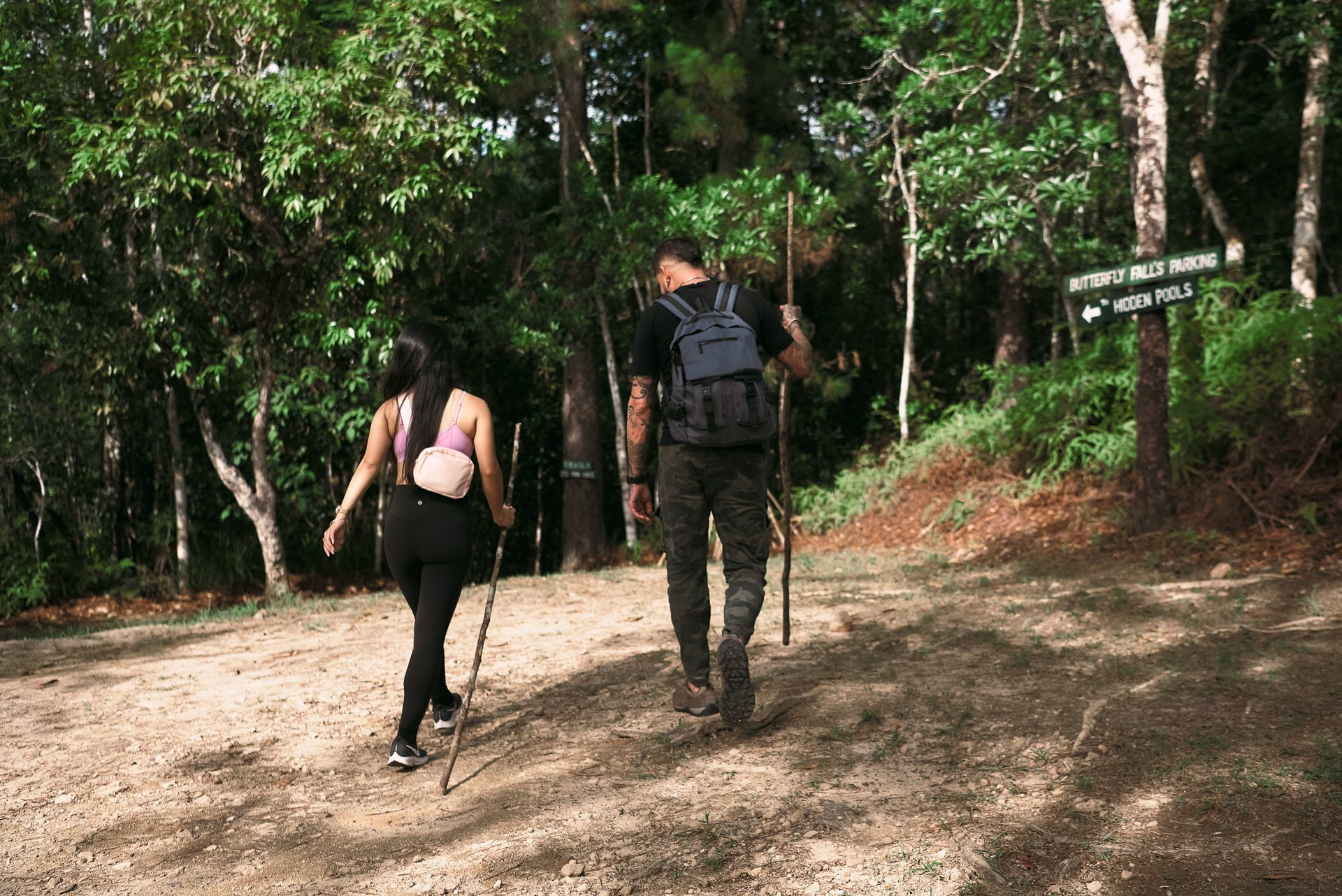 A man and a woman are walking down a dirt path in the woods.