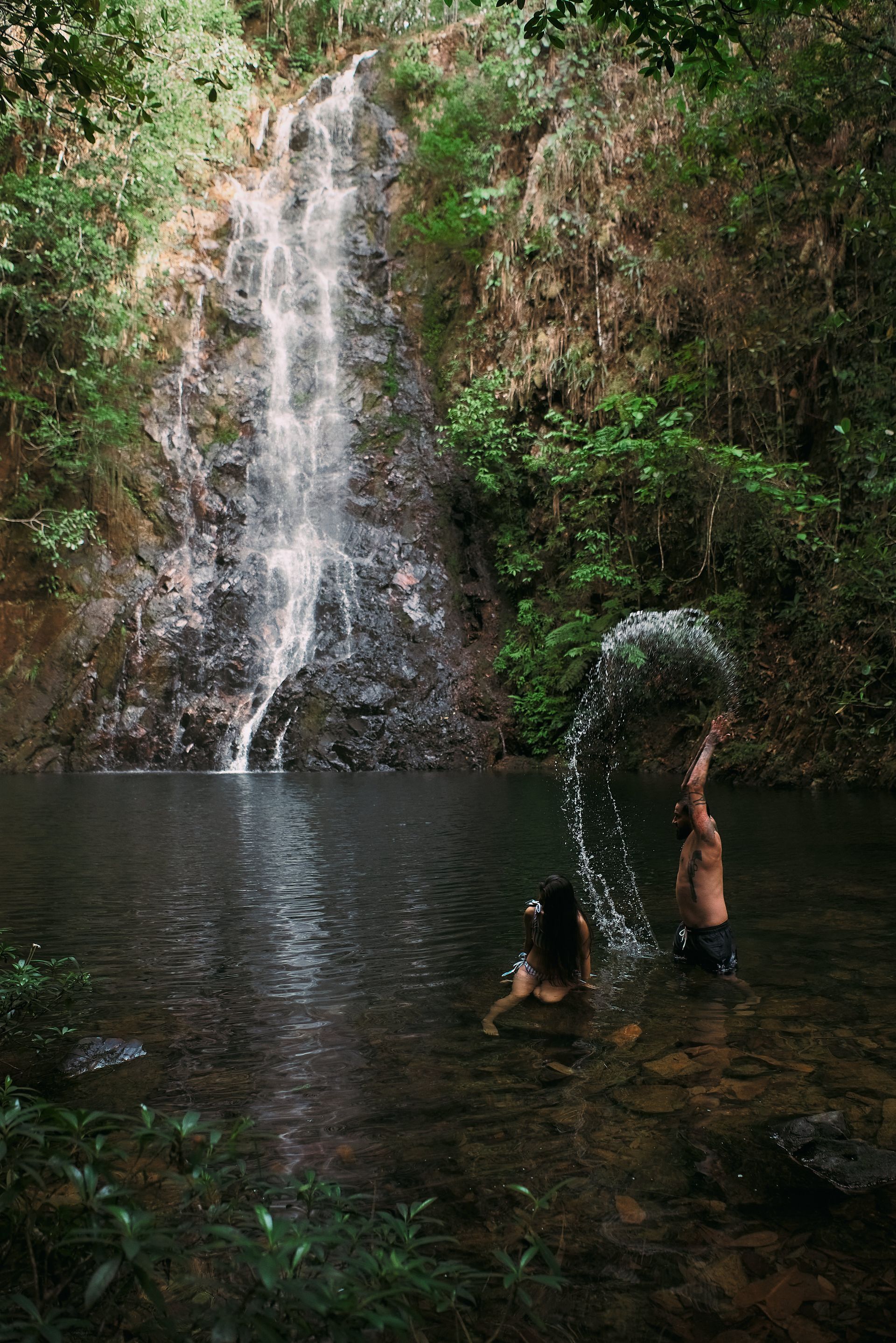 A man and a woman are playing in a waterfall.