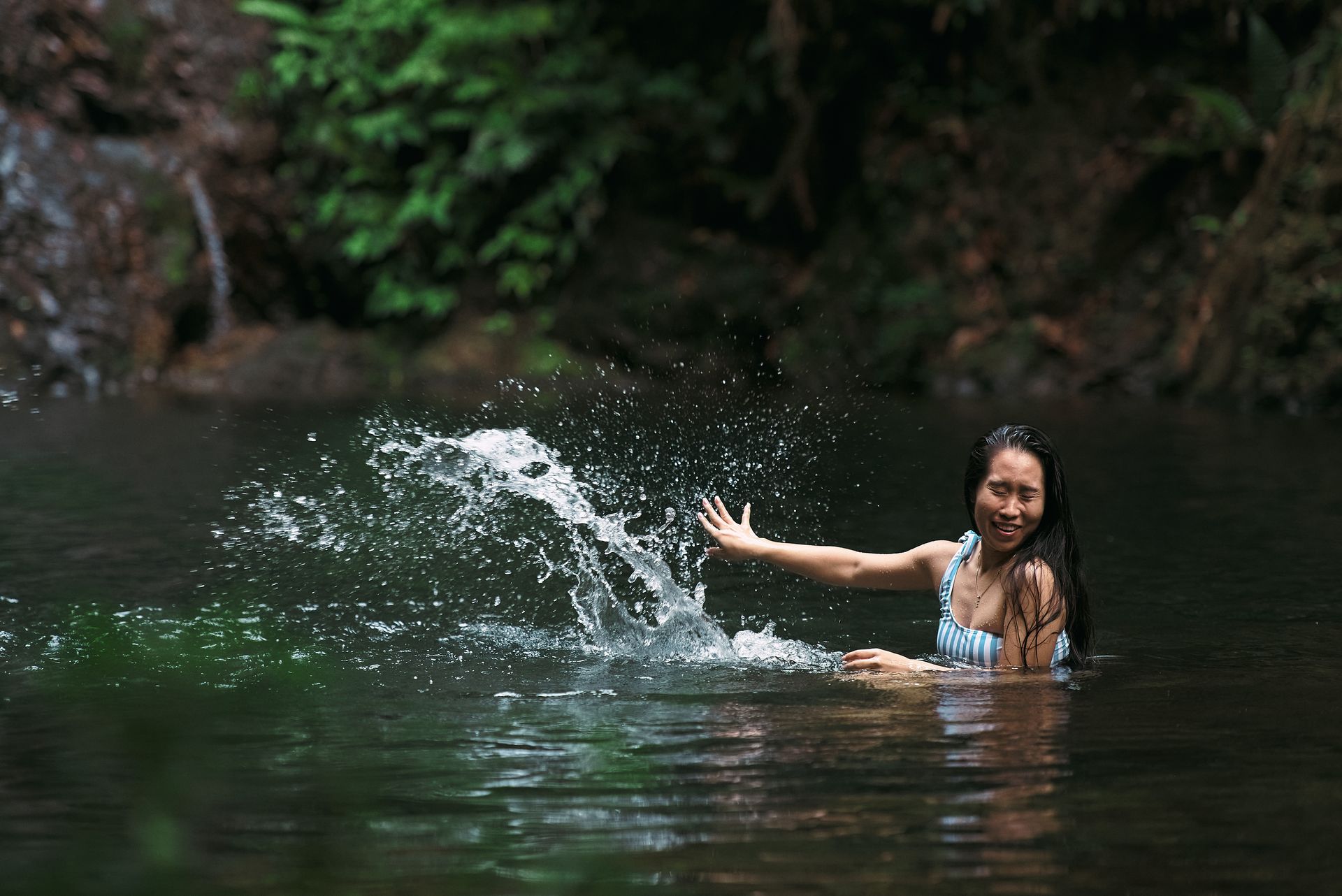 A woman in a bikini is splashing in a river.