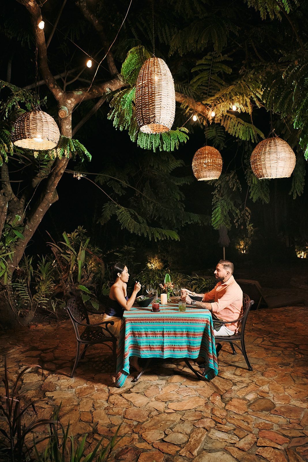 A man and a woman are sitting at a table under a tree at night.