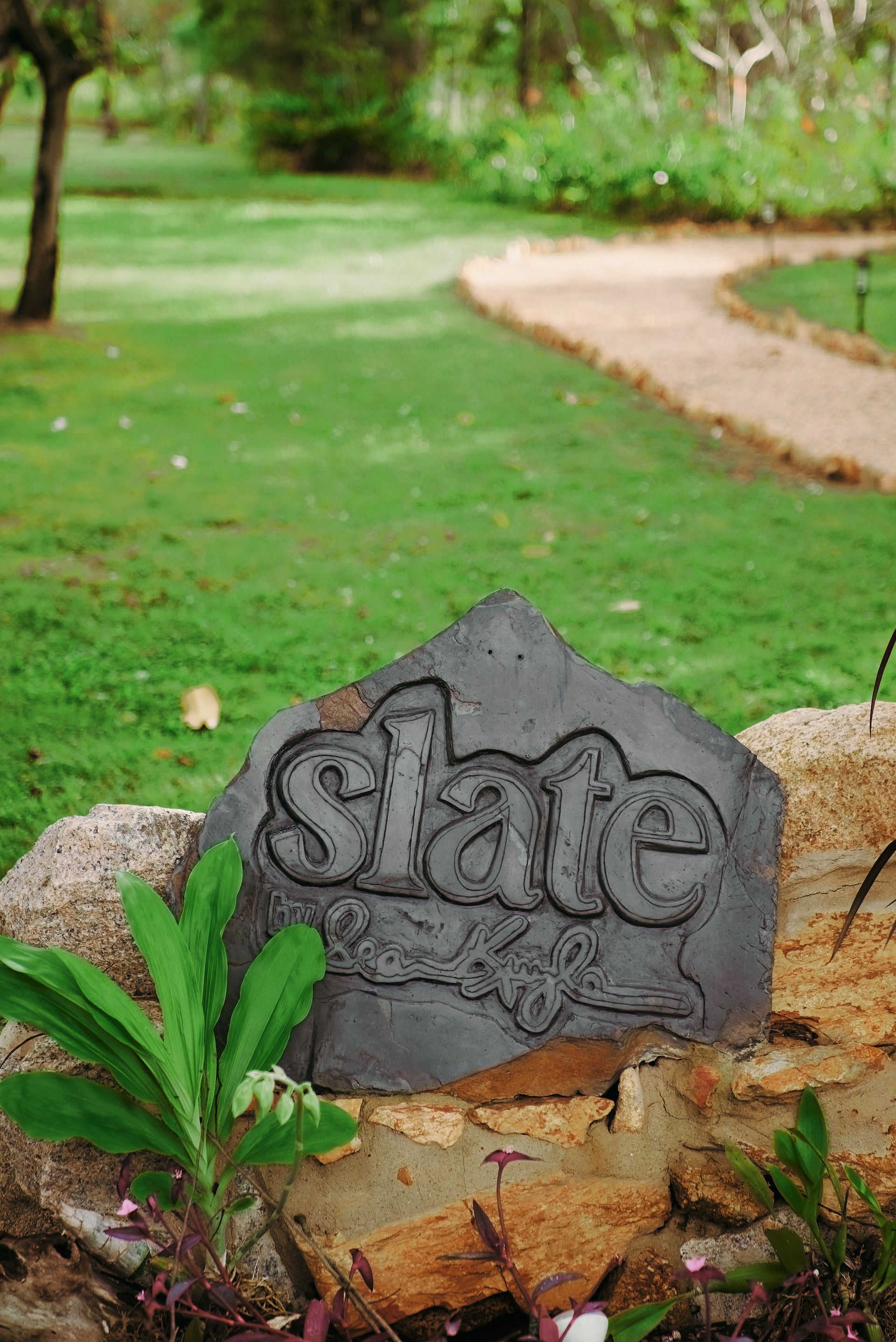 A stone with the word slate carved into it is in a garden.