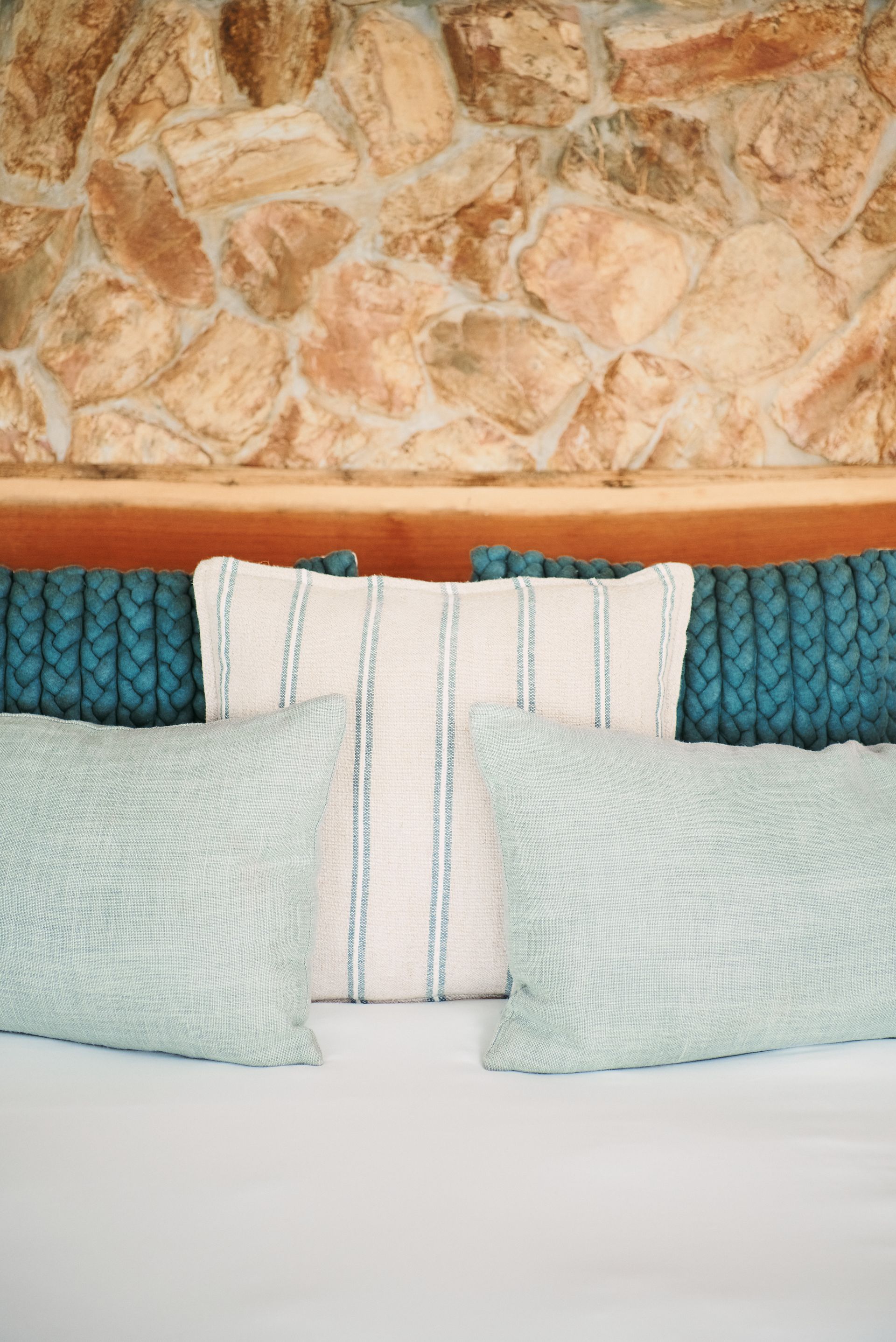 A bed with three pillows on it in front of a stone wall.