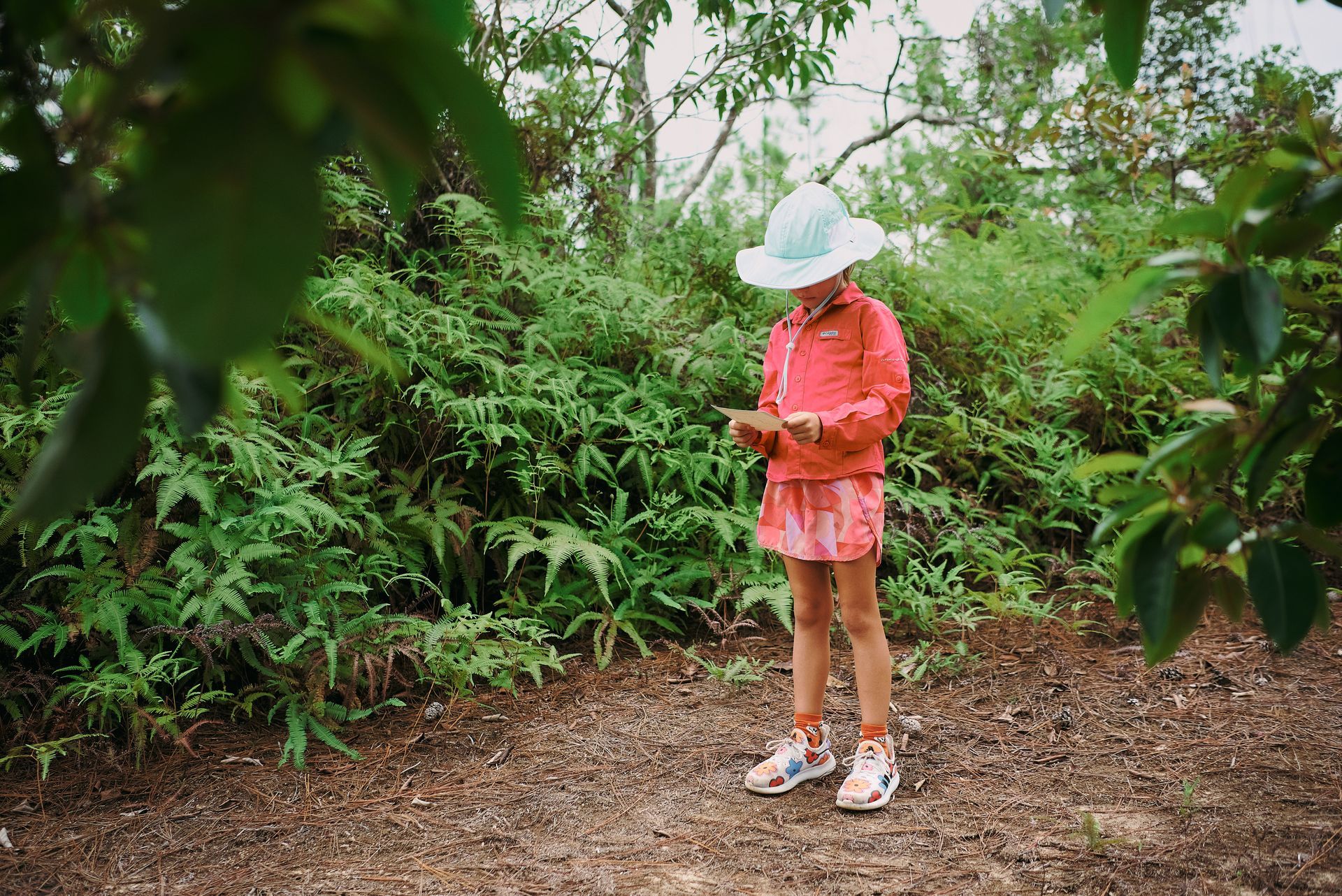 A little girl is standing in the woods looking at her phone.