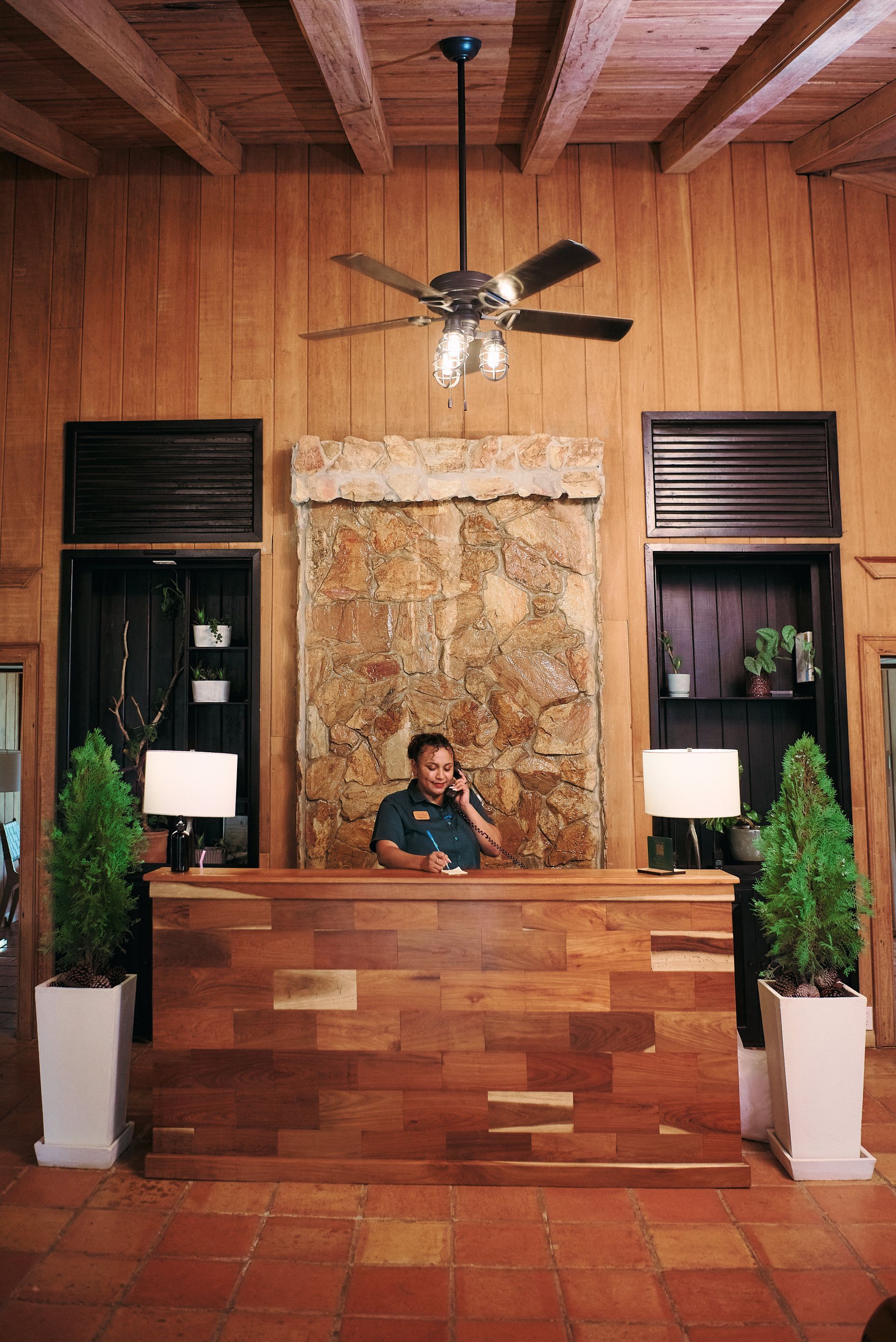 A man is standing behind a wooden desk in a room with a ceiling fan.