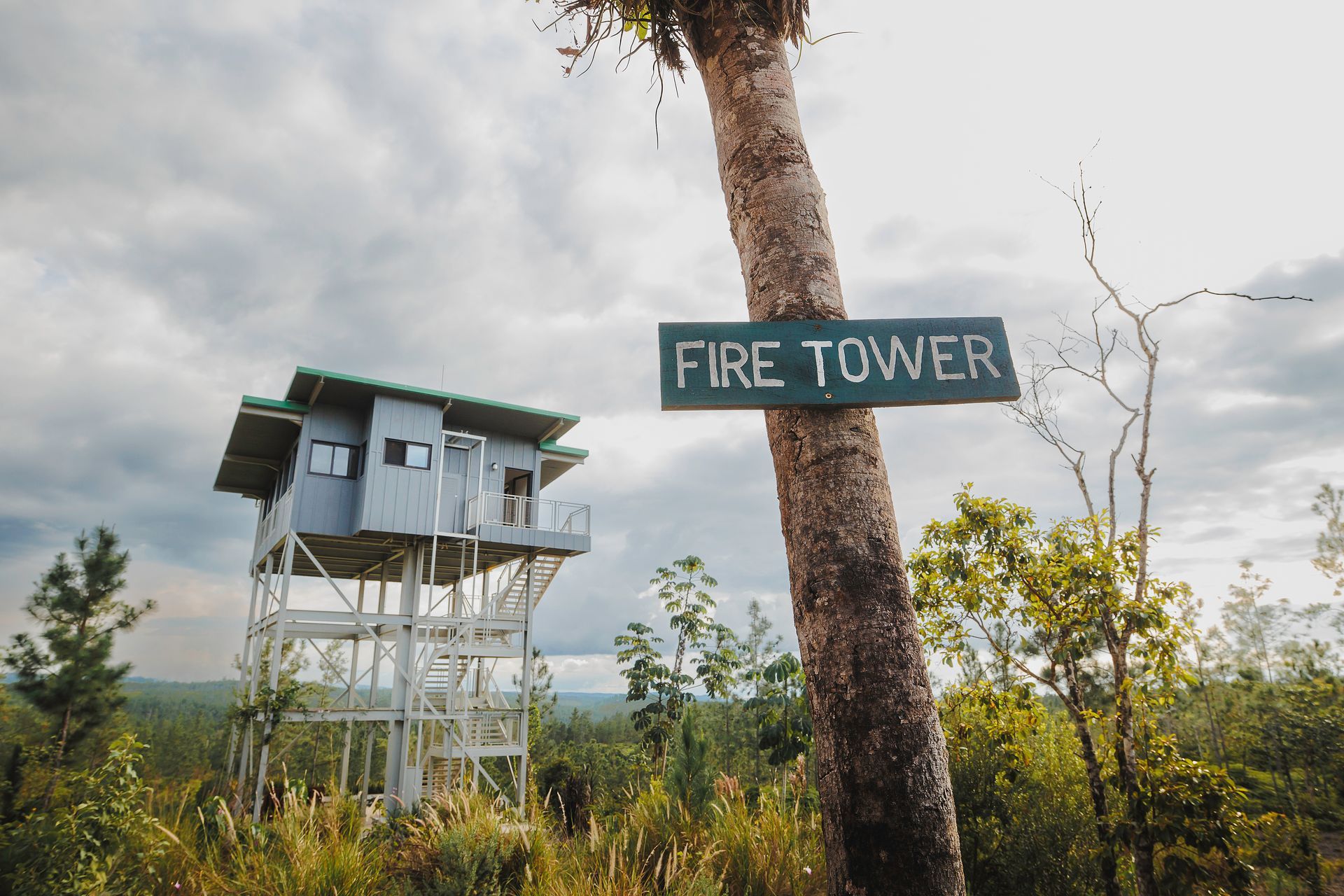 Fire tower in a wooded area with a sign attached to a tree. Eco Lodge