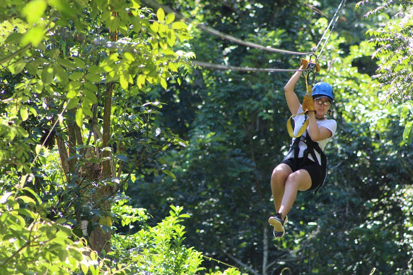 A woman is flying through the air on a zip line in the woods.