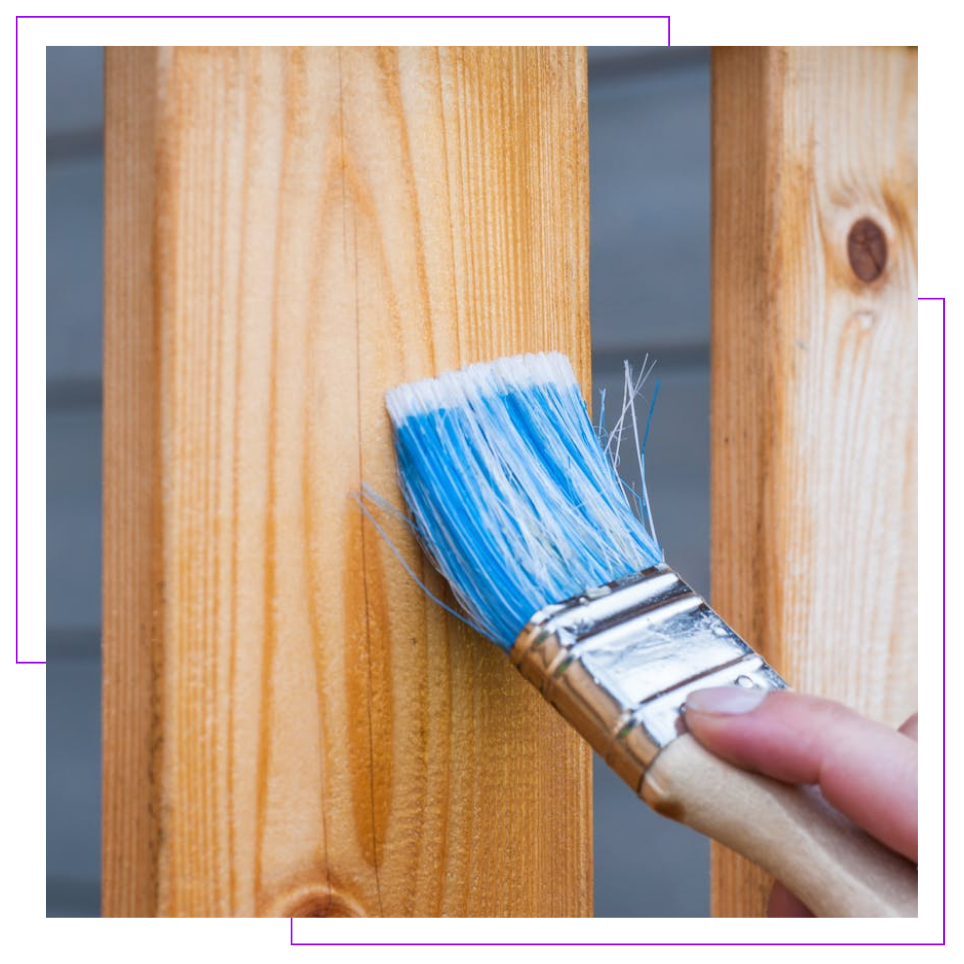 A person is painting a wooden post with a blue brush.