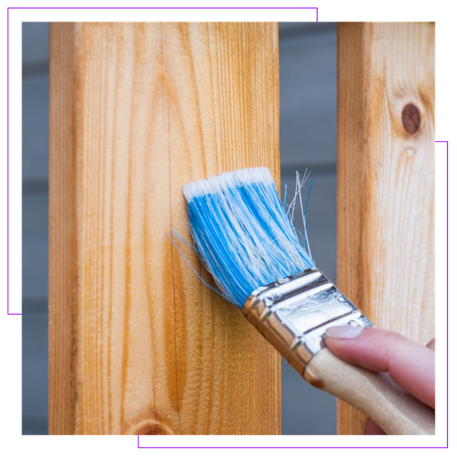 A person is painting a wooden post with a blue brush.