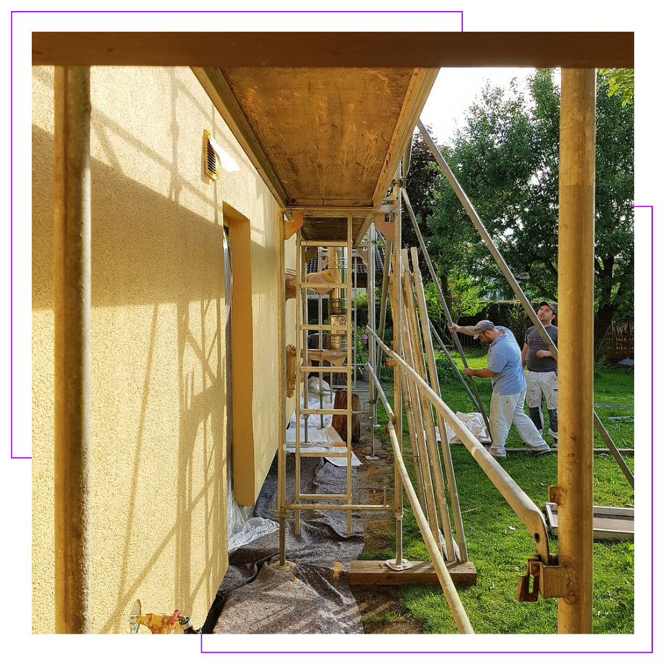 A man is painting the side of a building on a scaffolding.