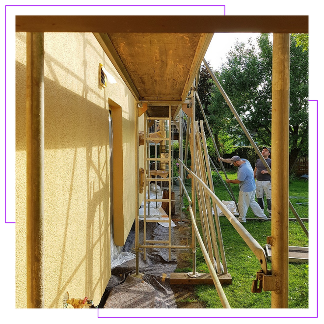 A man is painting the side of a building on a scaffolding.