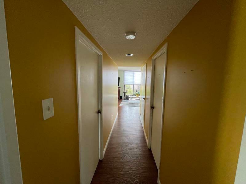 A long hallway with yellow walls and white doors leading to a living room.