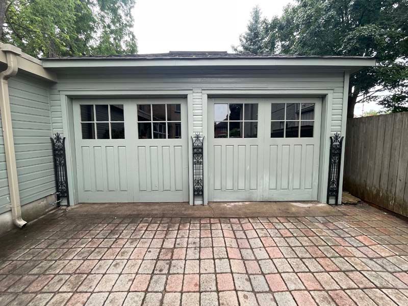 A garage with two garage doors and a brick driveway.