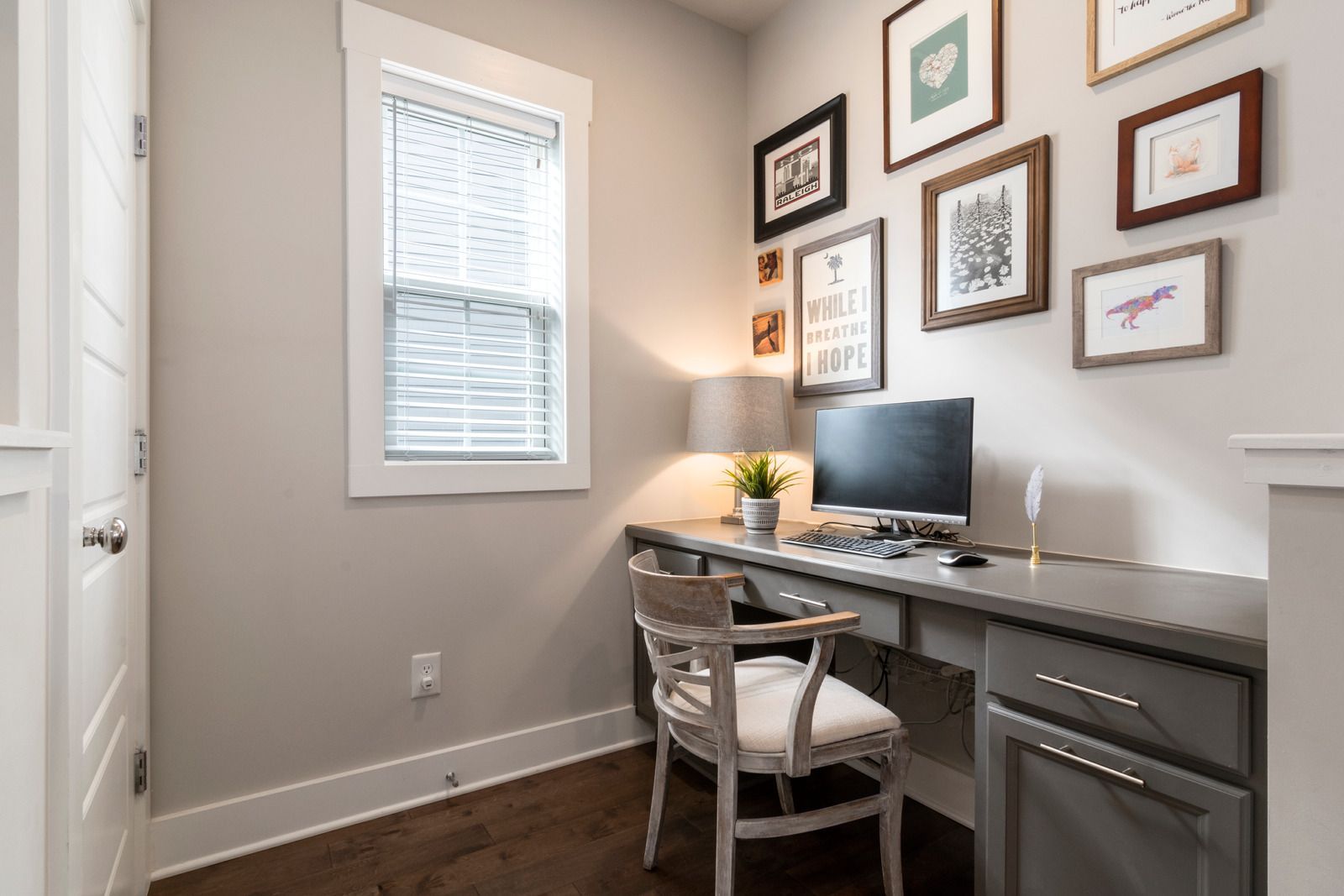 A home office with a desk , chair , computer and pictures on the wall.