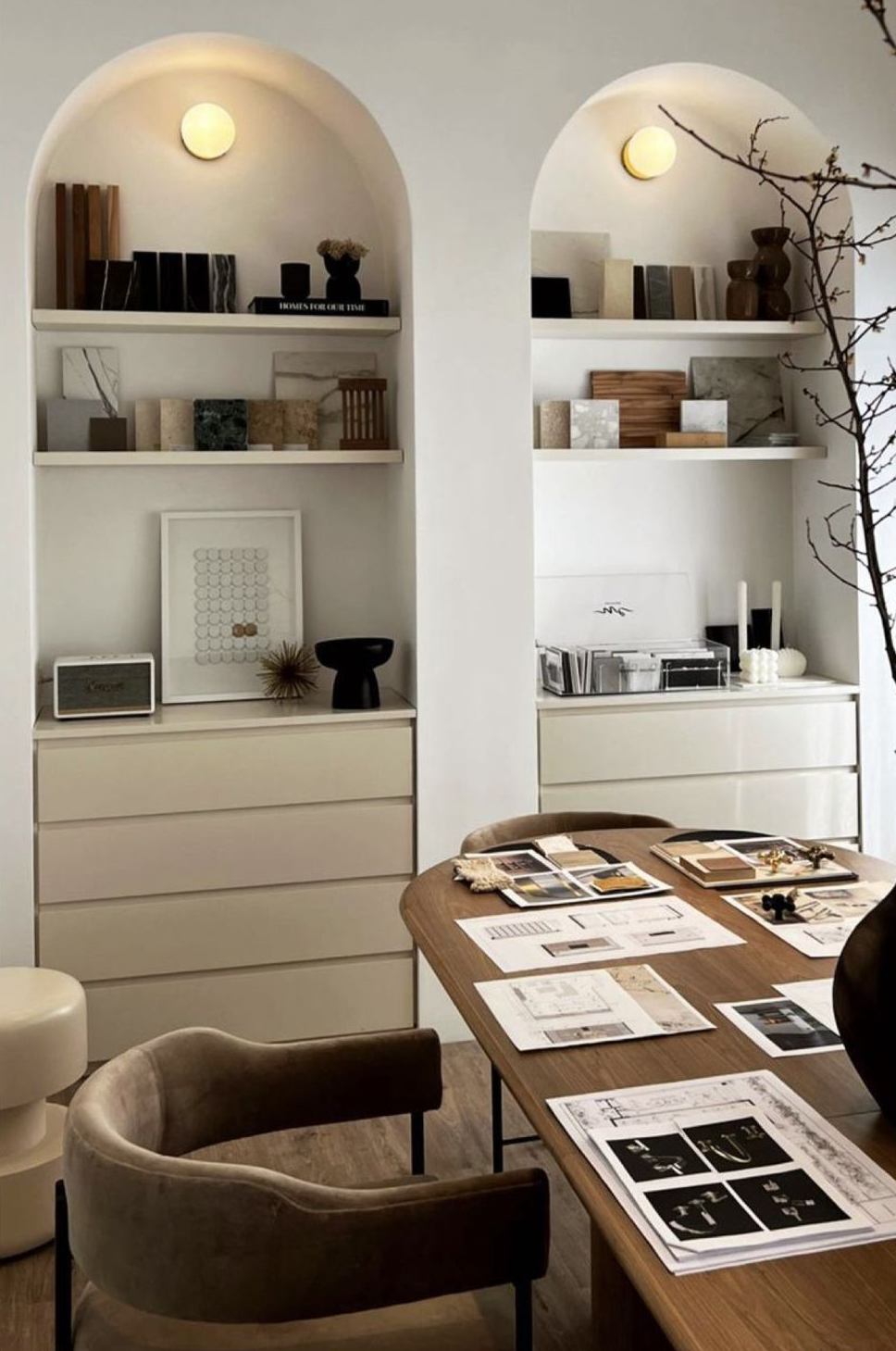 Dos nichos de pared blancos con arcos, estantes, iluminación tenue y elementos decorativos sobre cómodas minimalistas