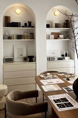 Dos nichos de pared blancos con arcos, estantes, iluminación tenue y elementos decorativos sobre cómodas minimalistas