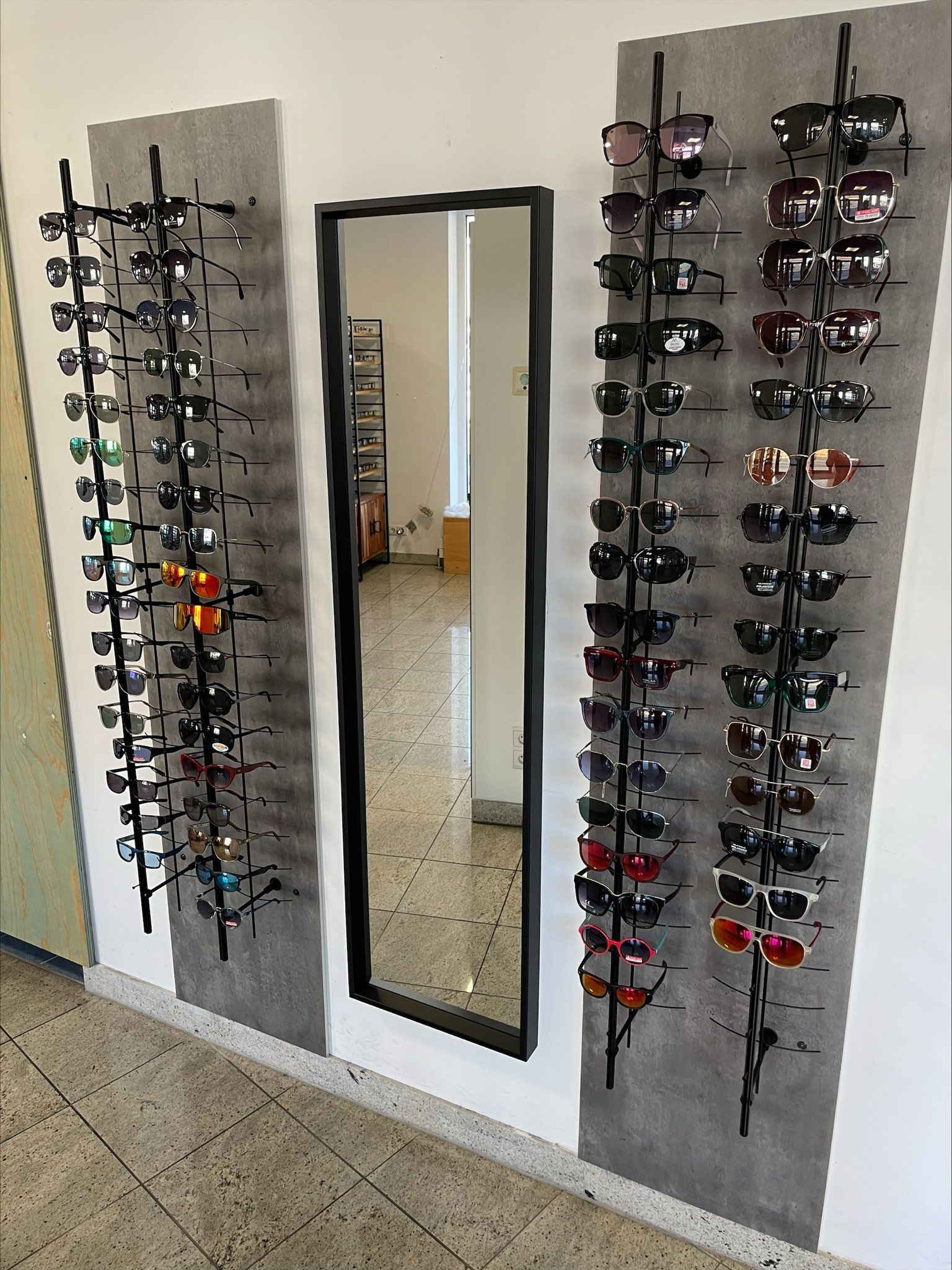 eine Reihe von Sonnenbrillen hängt an einer Wand neben einem Spiegel .