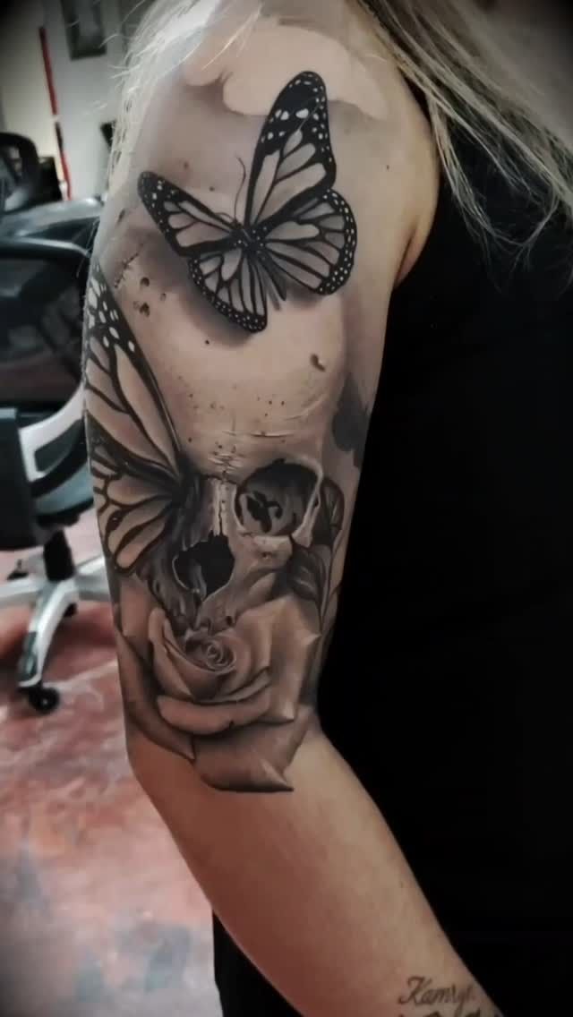 A woman has a tattoo of a skull and butterflies on her arm.