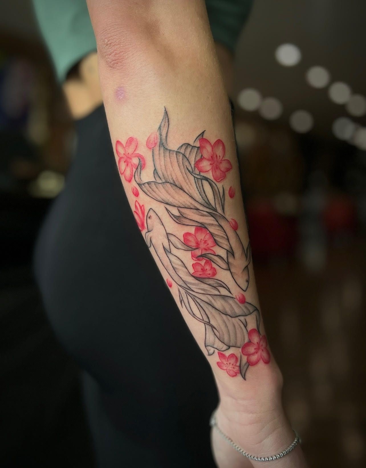 A woman has a tattoo of fish and flowers on her forearm
