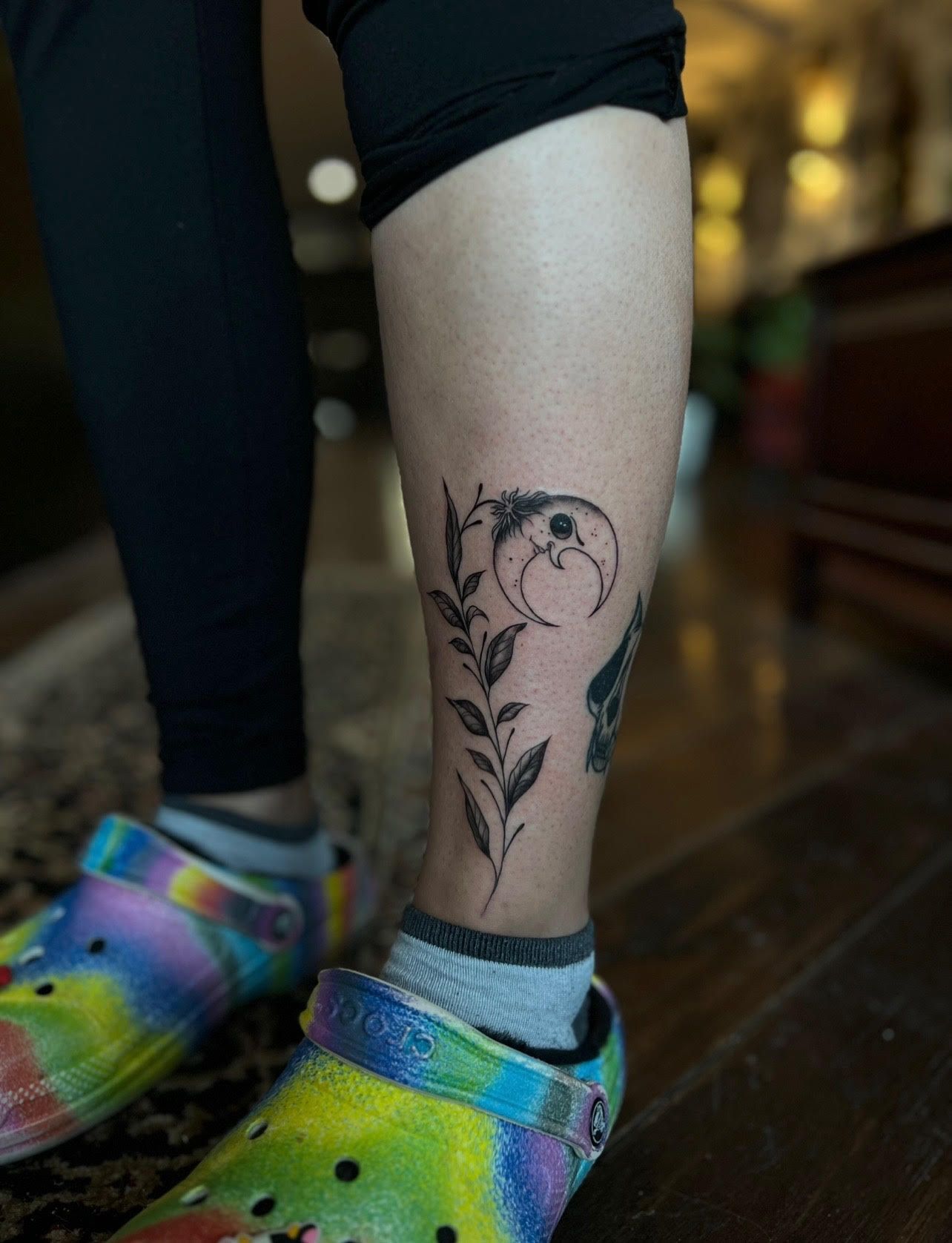 A person with a tattoo on their leg wearing tie dye crocs.