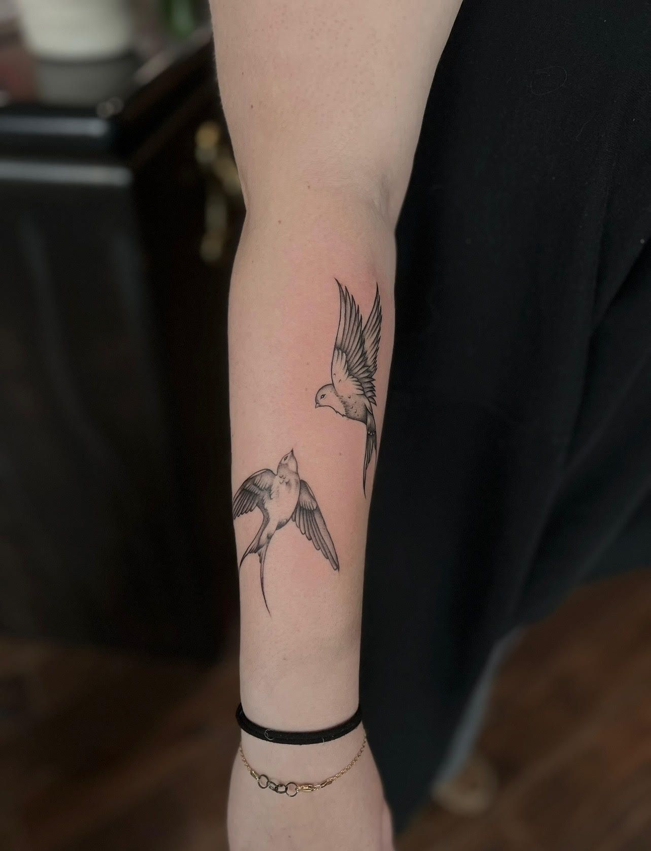 A woman has a tattoo of two birds on her forearm