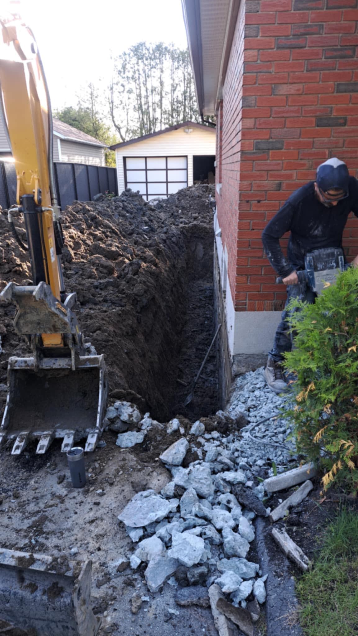 Un homme creuse un trou dans le sol à côté d'un bâtiment en briques.