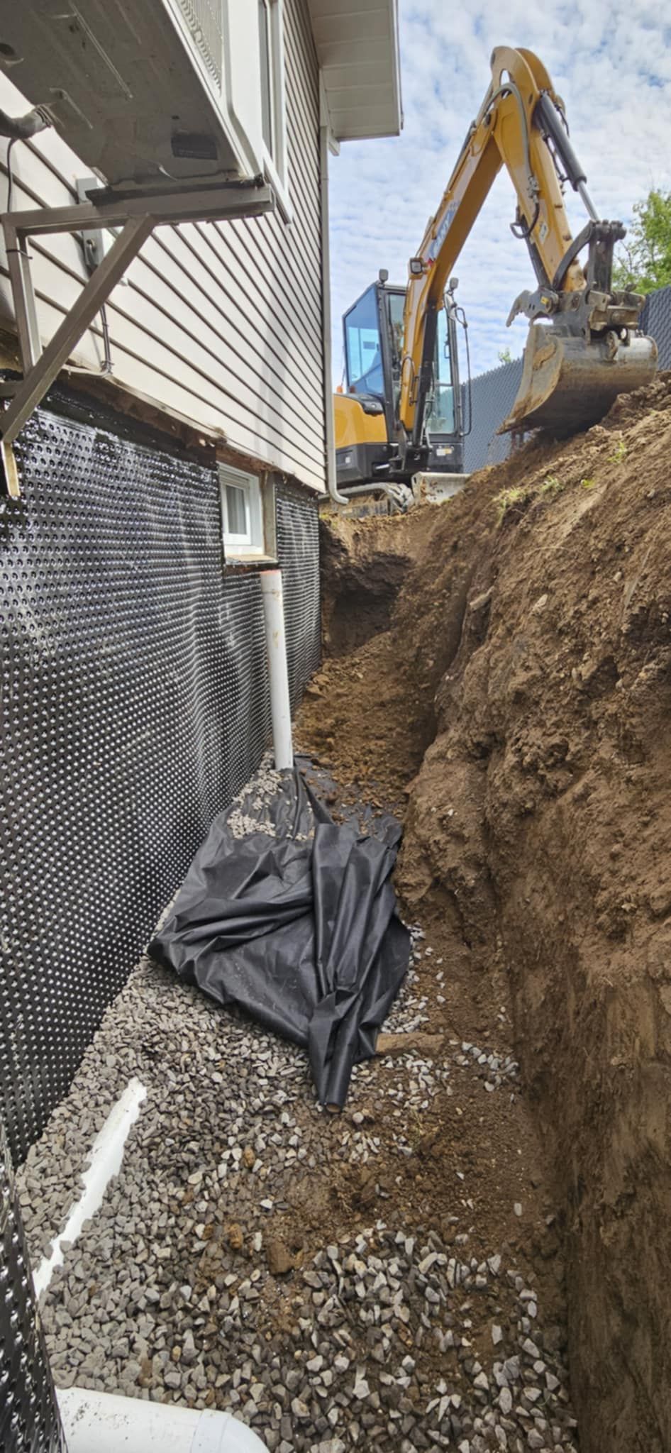 Une excavatrice jaune creuse un trou devant une maison.