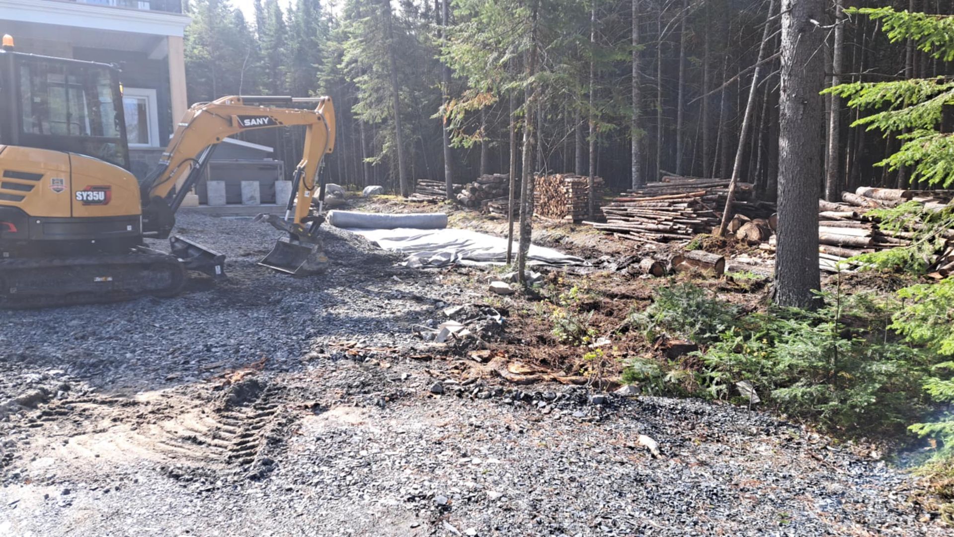 Une excavatrice jaune roule sur un chemin de terre au milieu d'une forêt.