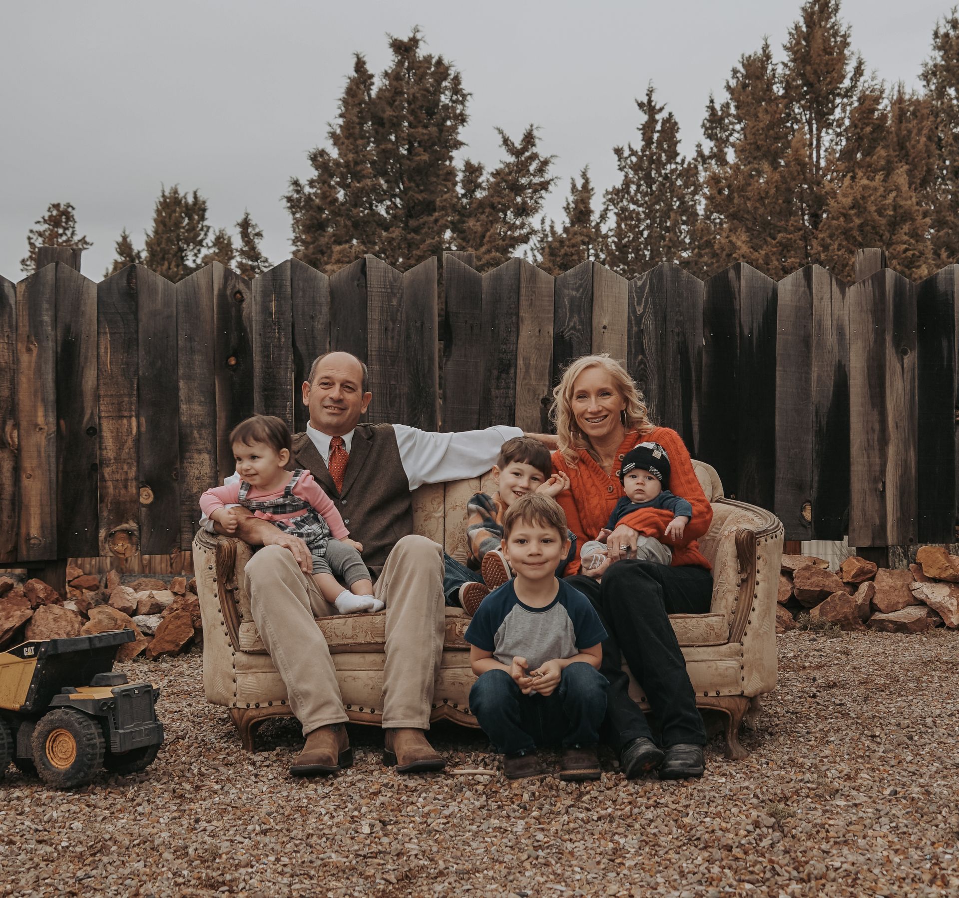 Family of six on an old couch in a yard; cloudy day.