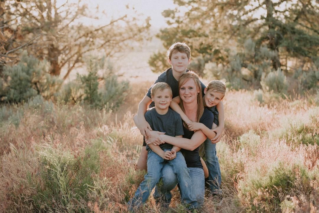 Woman and three boys pose in a field, embracing. Warm tones, smiling faces.