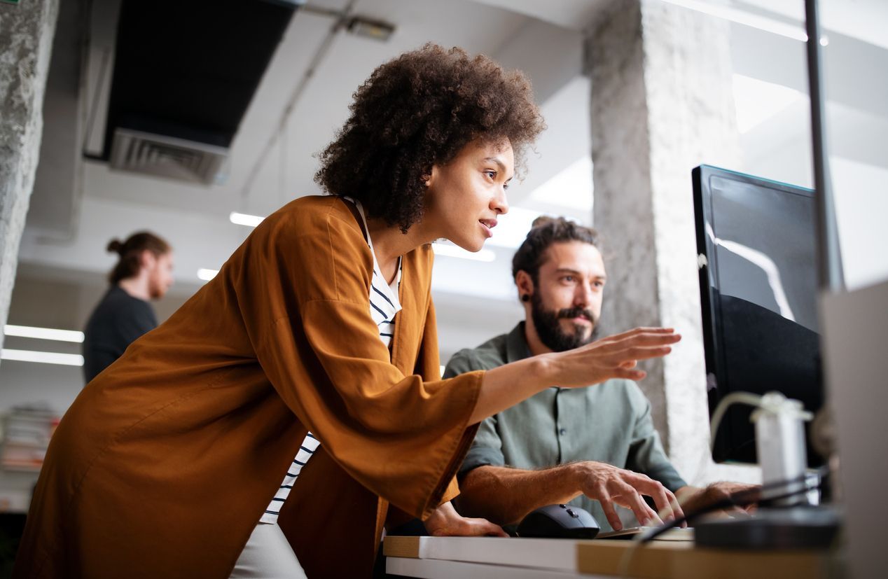 A woman is standing next to a man looking at a computer screen.
