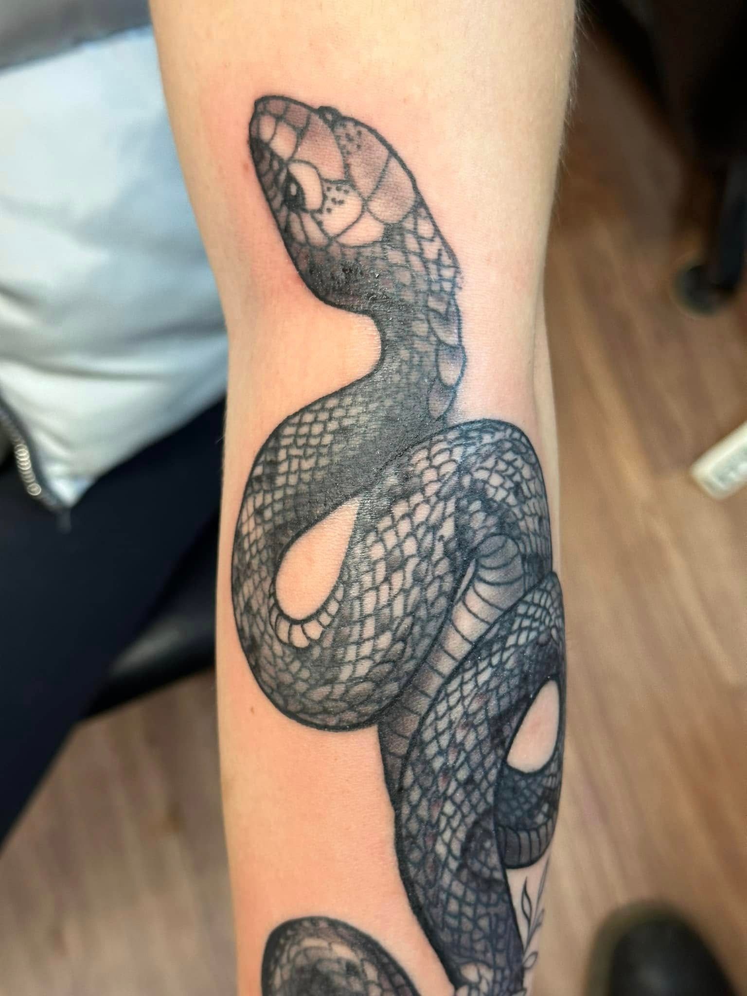 Black and gray snake tattoo coiled around an arm, detailed with scale patterns and eye details.