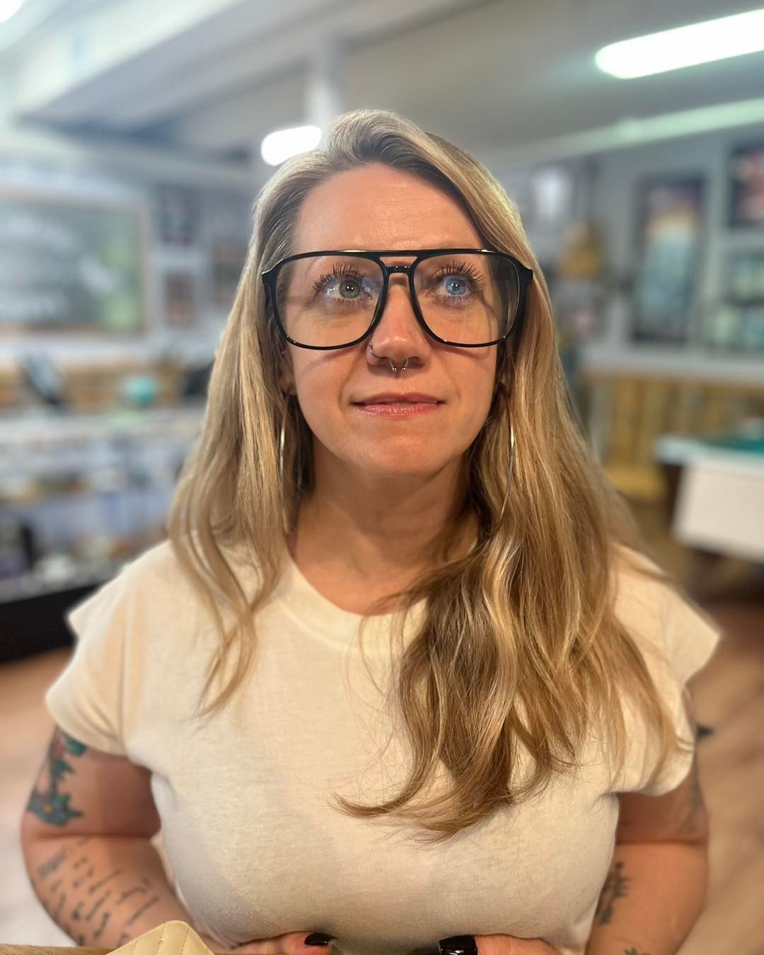 Woman wearing large glasses, looking upwards, in a shop with displays.