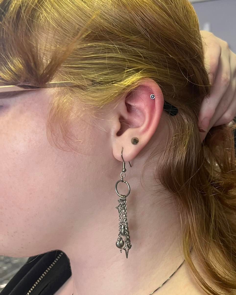 Person's ear with multiple piercings, including a long, dangling earring. Light skin and reddish-blonde hair.