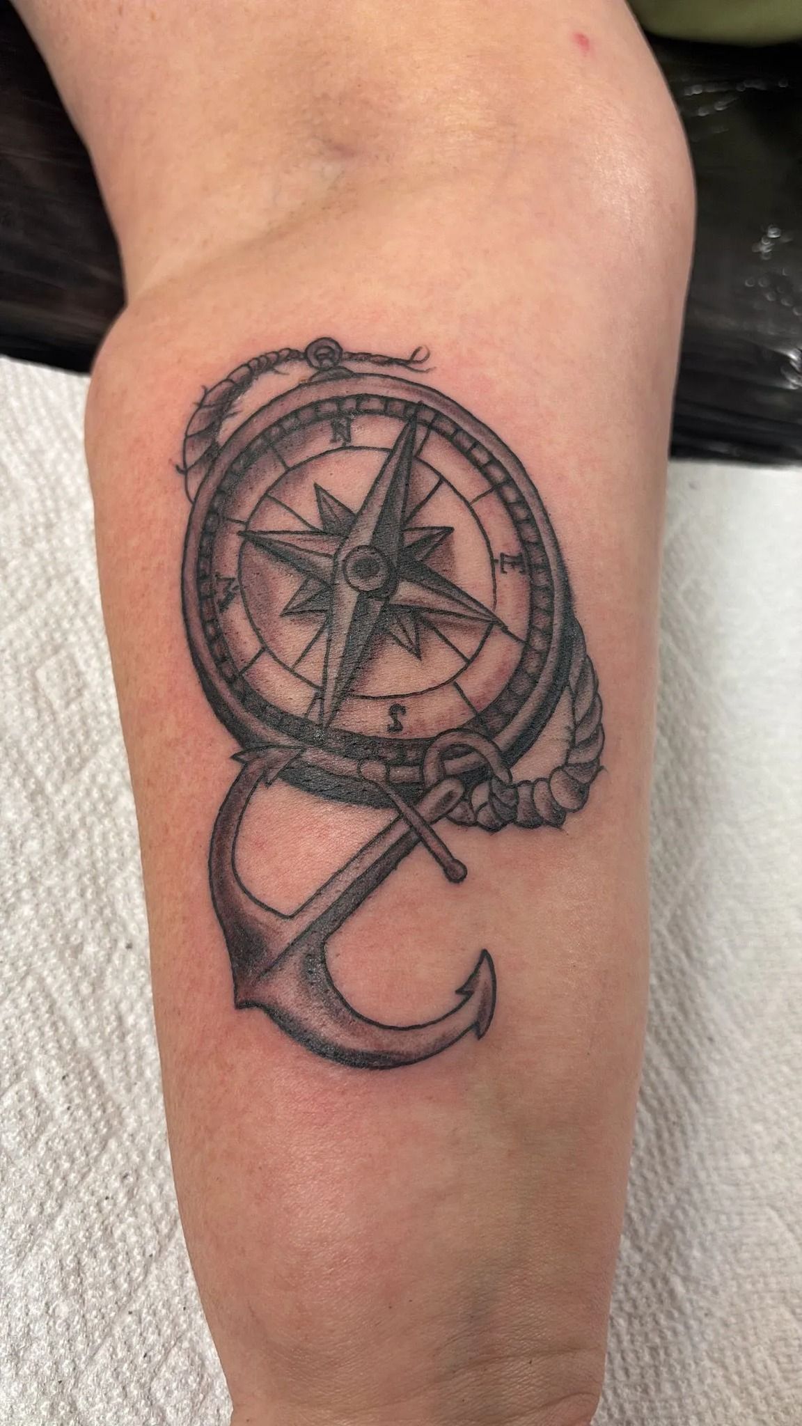 Tattoo of a compass rose atop an anchor, with rope detailing; grayscale on an arm.