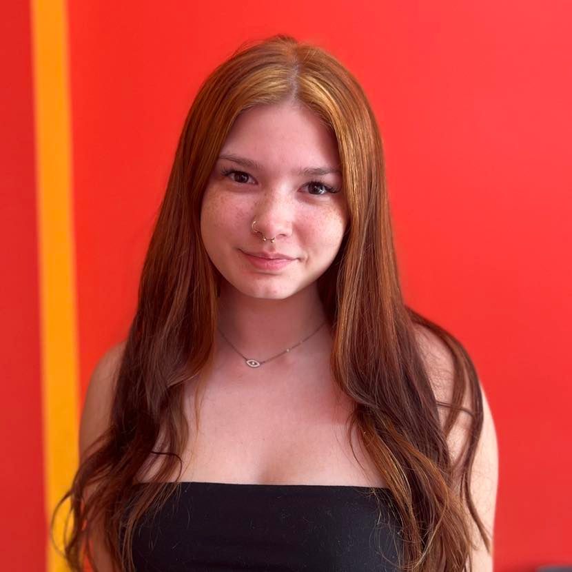 Young person with curly dark hair, wearing a white shirt and backpack, looking off to the side. Inside a building.