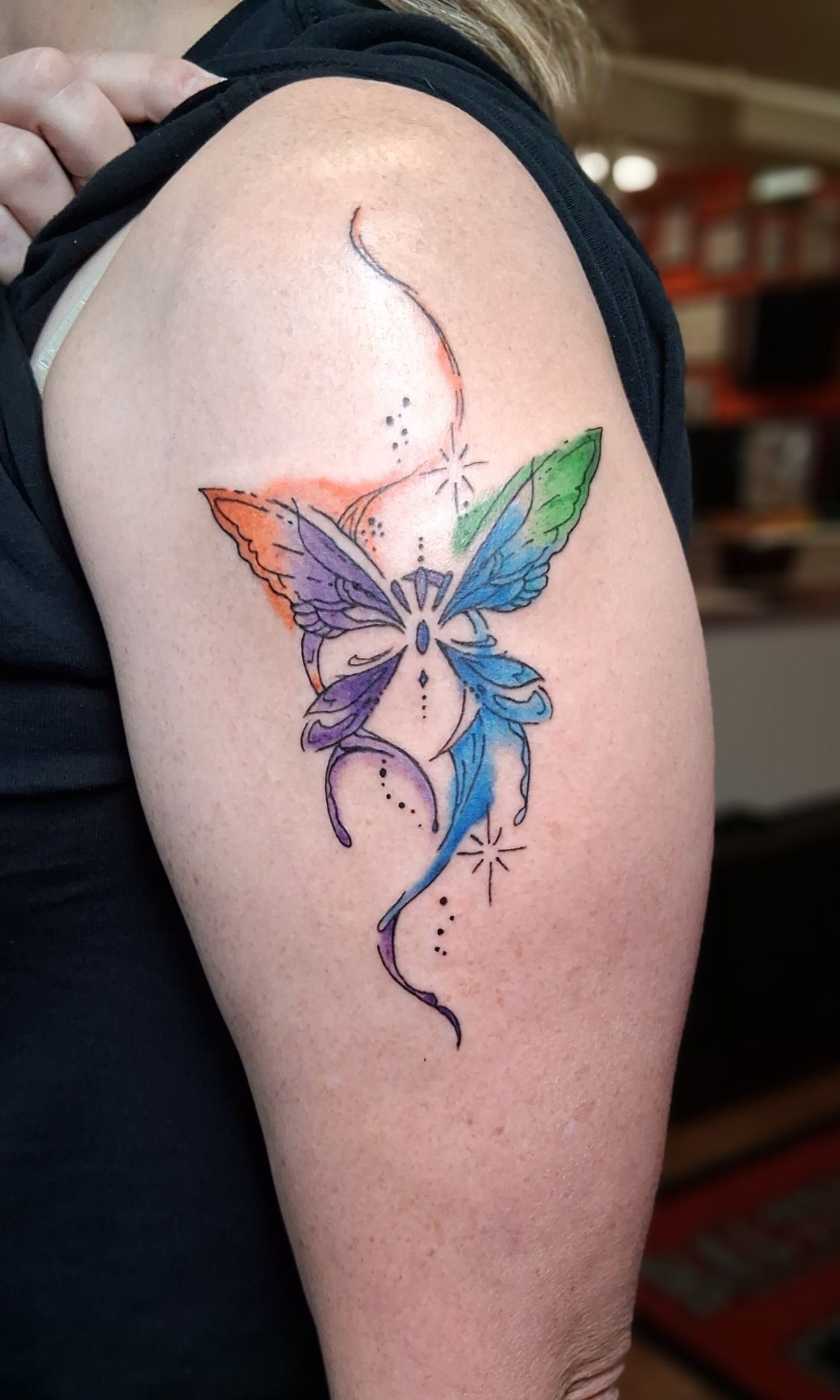Tattoo on an arm: watercolor butterfly with purple, green, orange, and blue wings; stars and stems.