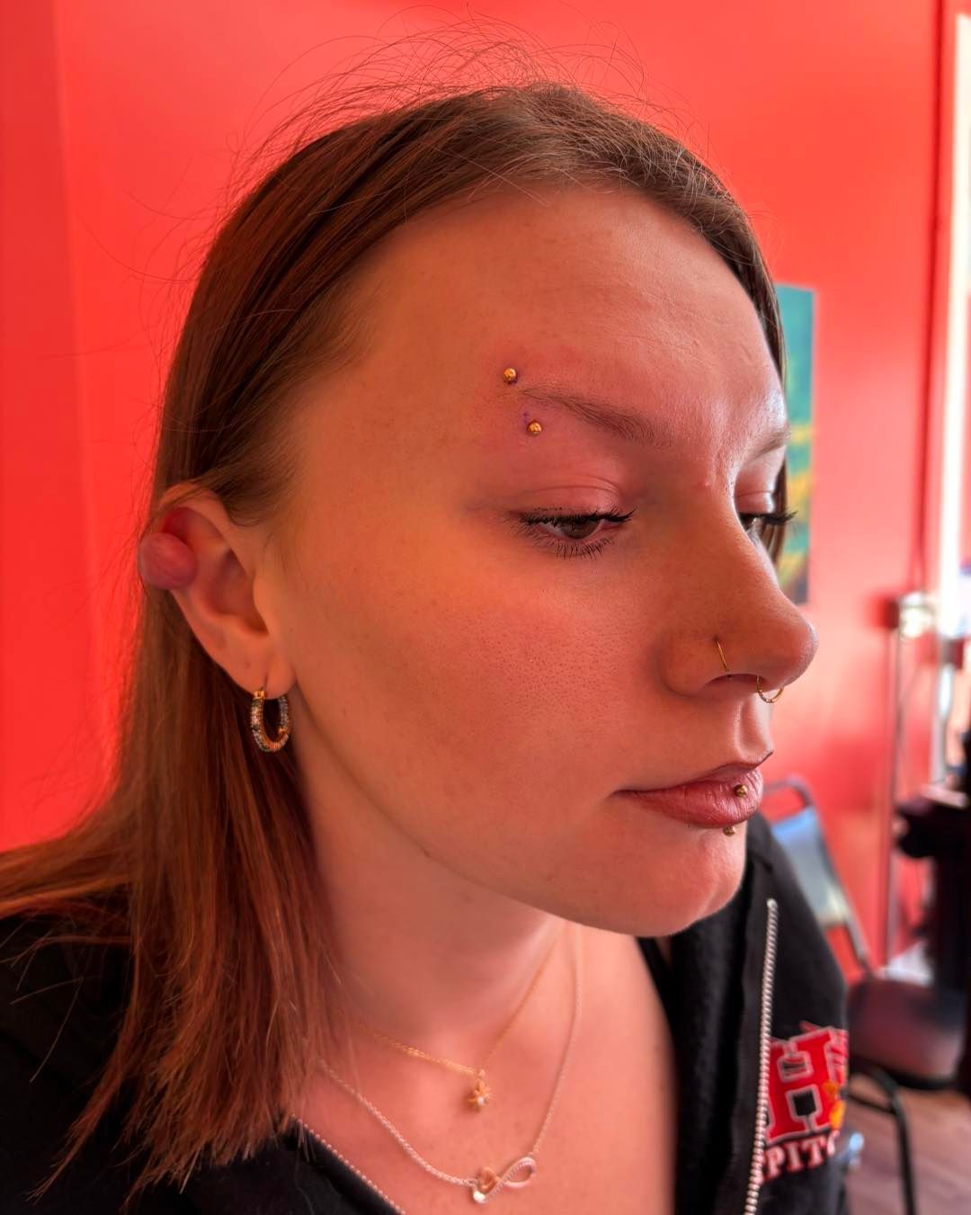 Woman with braided hair, wearing a pink hoodie, and silver hoop earrings, in a room with displays.