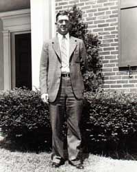 A man in a suit and tie is standing in front of a brick building.