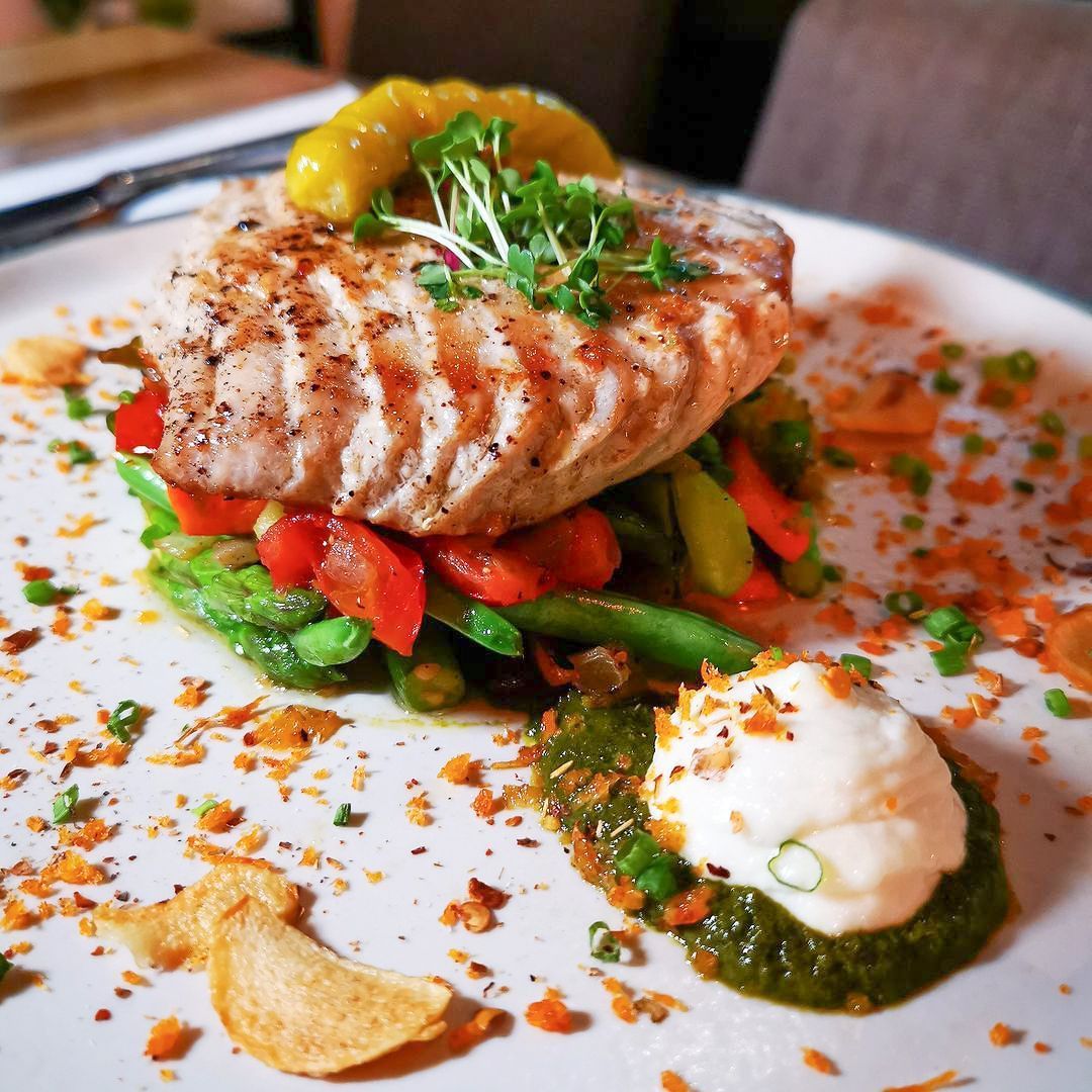 A white plate topped with a piece of meat and vegetables