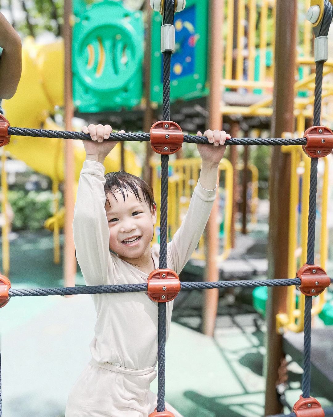 A young boy is playing on a ropes course at a playground.