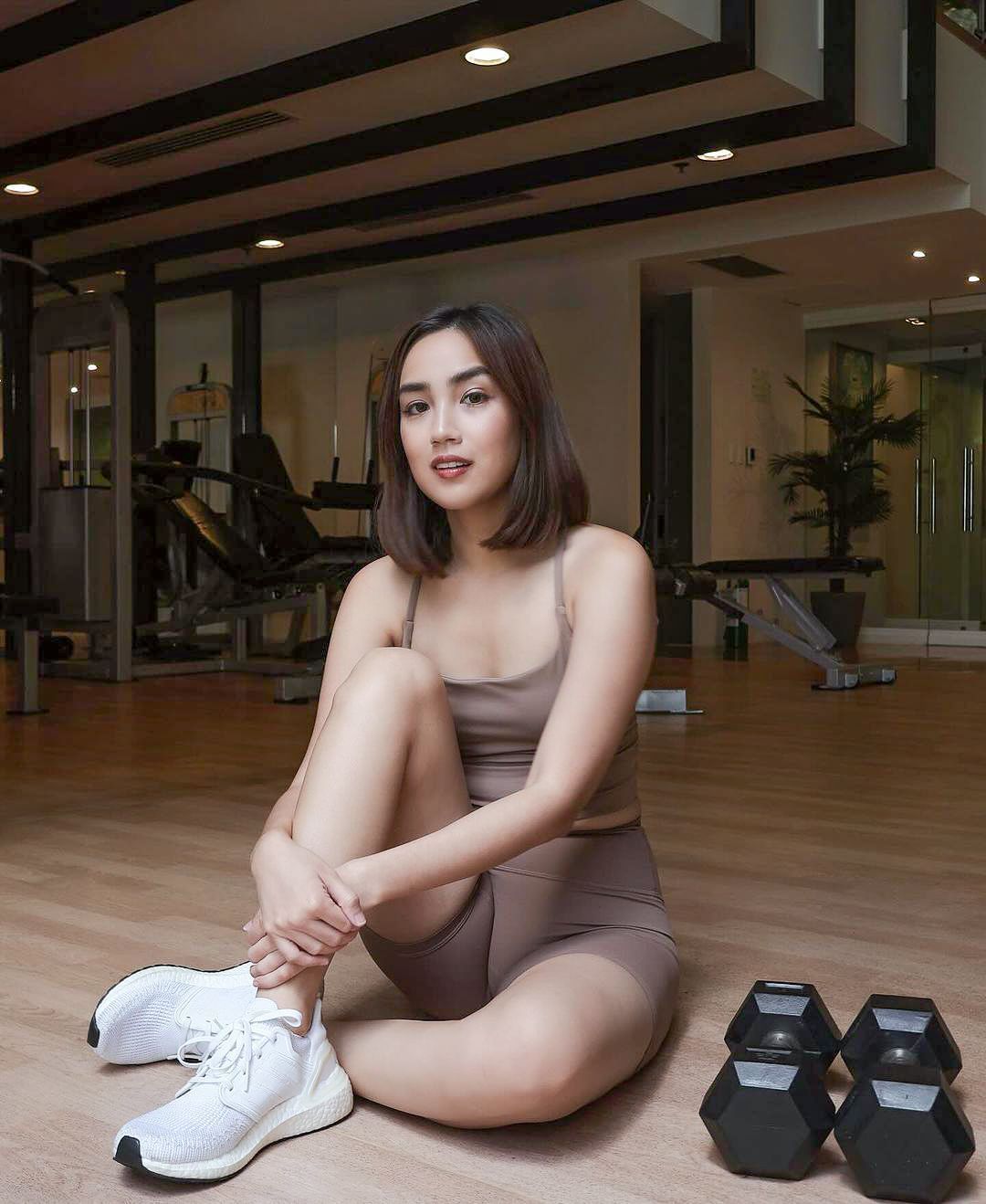 A woman is sitting on the floor in a gym next to dumbbells.