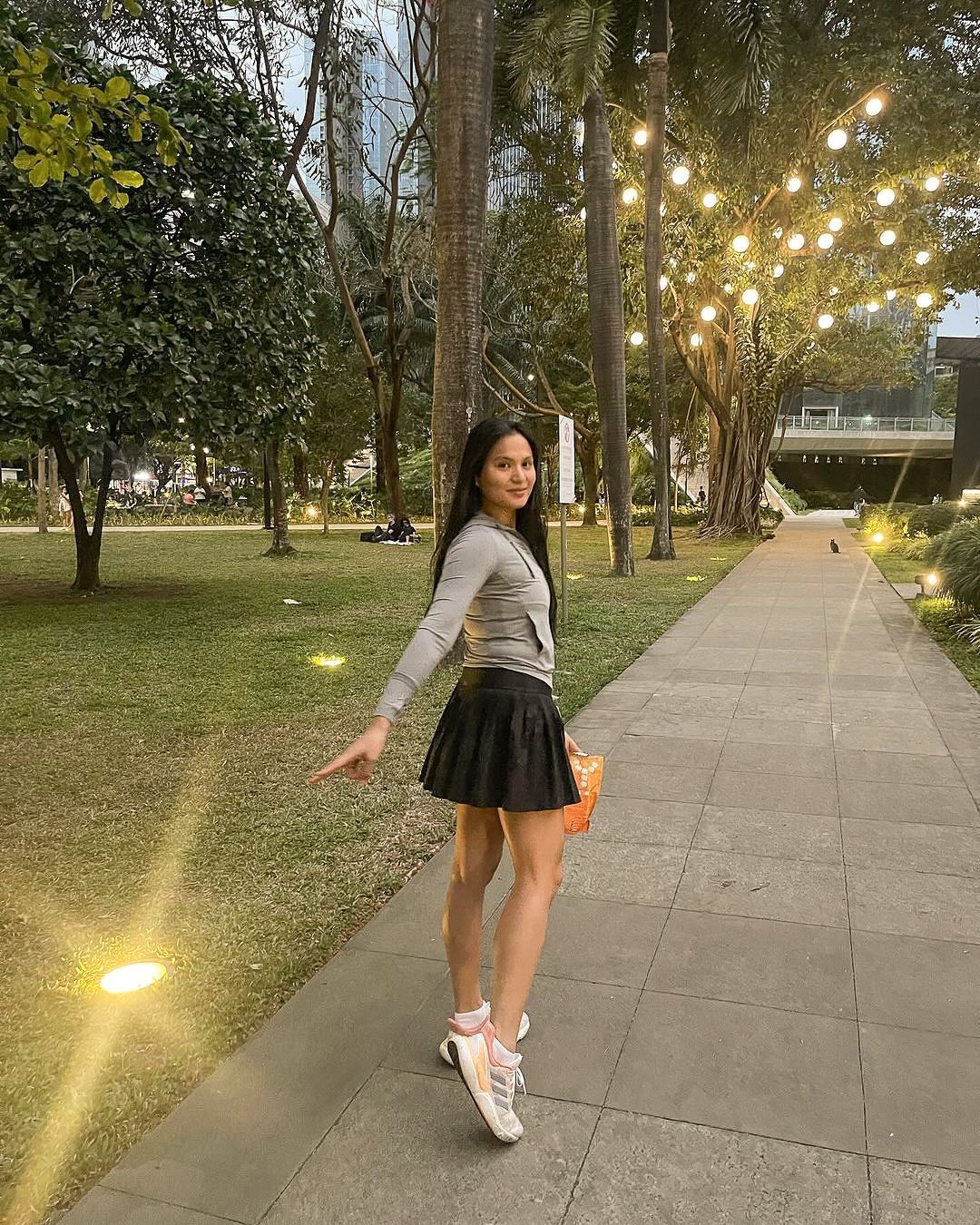 A woman is standing on a sidewalk in a park.