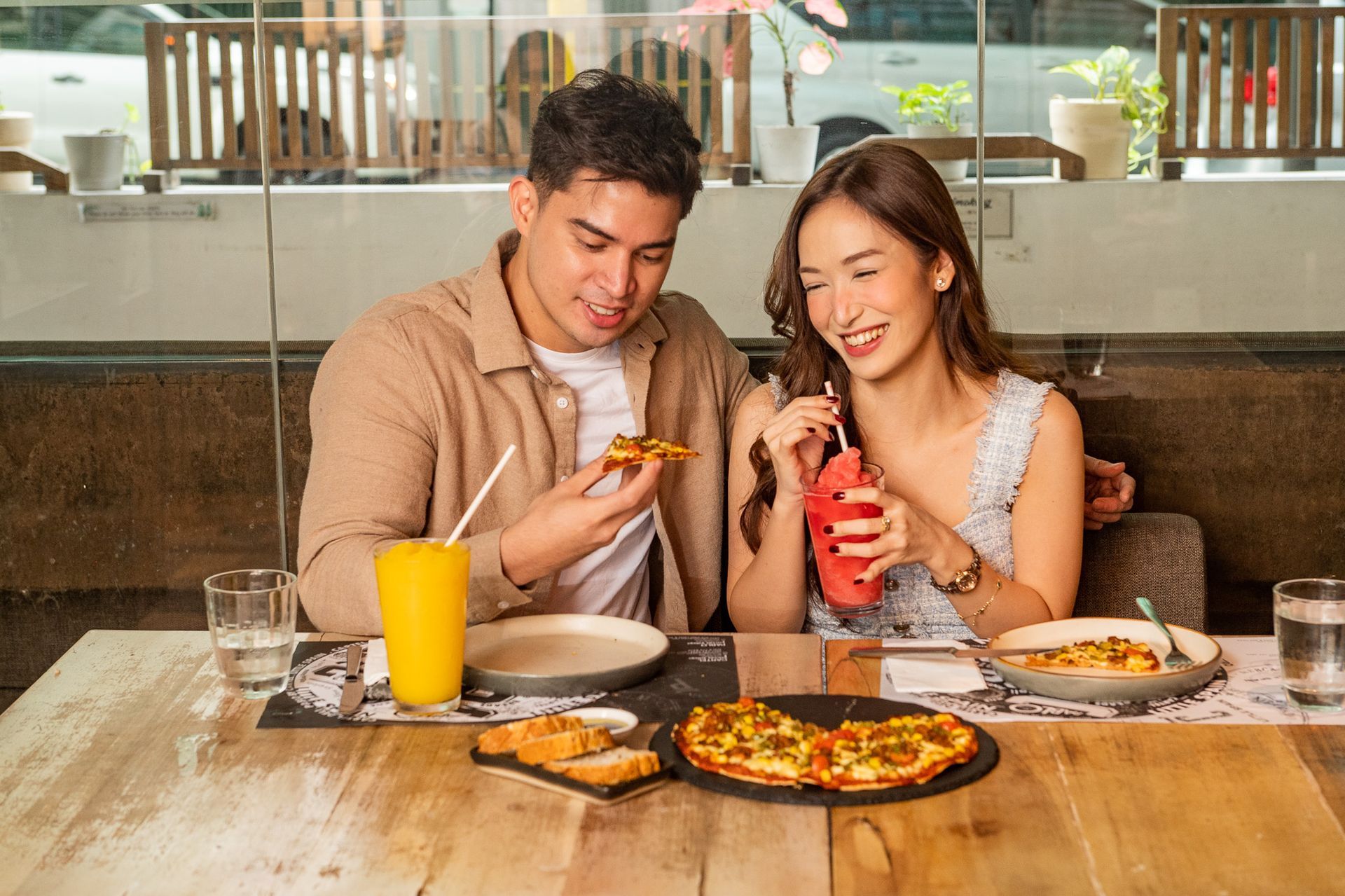 A man and a woman are sitting at a table eating pizza and drinking orange juice