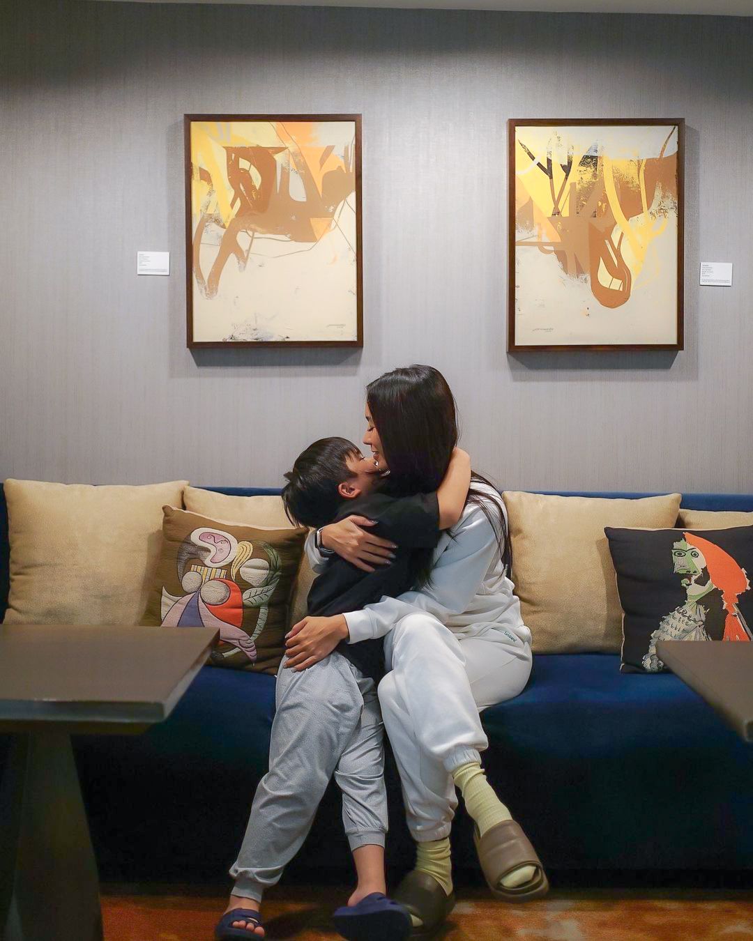 Woman hugging child on a blue sofa with artwork in the background.