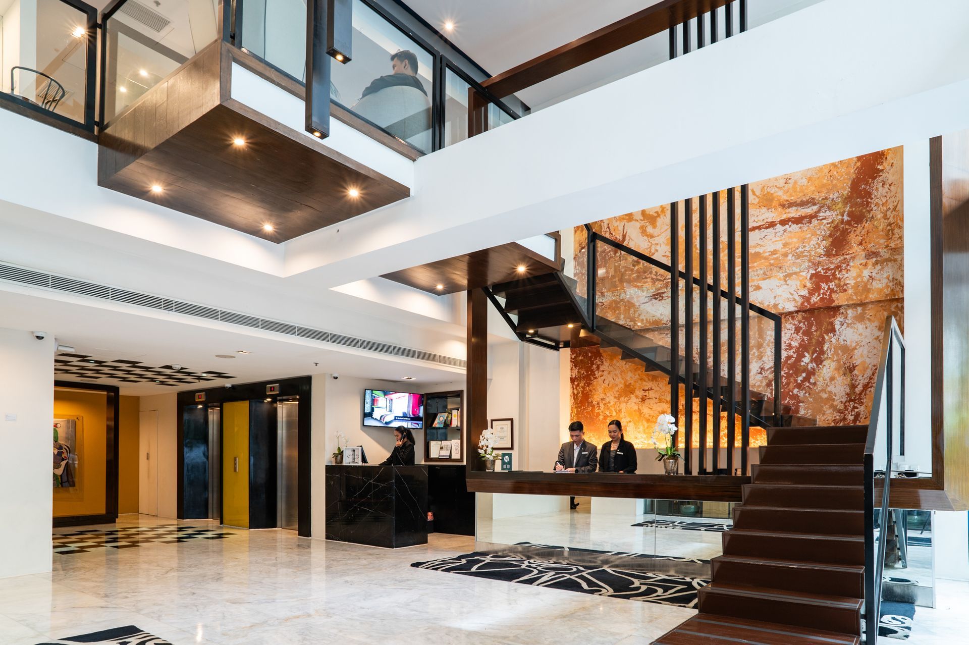 Hotel lobby with a front desk, stairs, and a decorative textured wall.